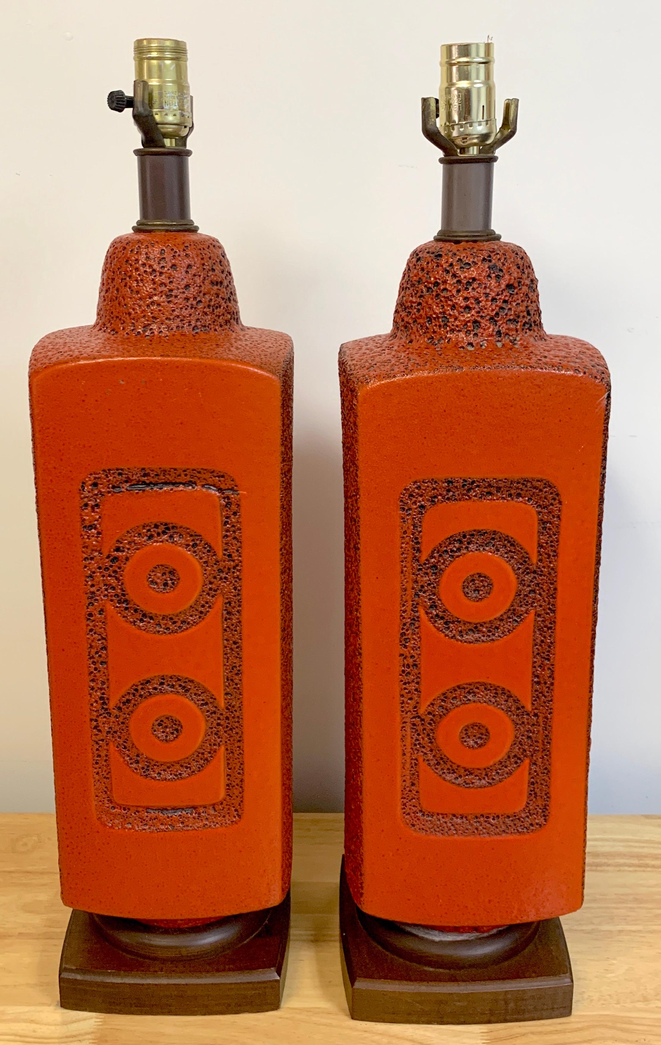 Pair of 1960s mod lava glazed orange lamps, each one with incised roundel and rectangle decoration front and back with rock work sides, raised on 6