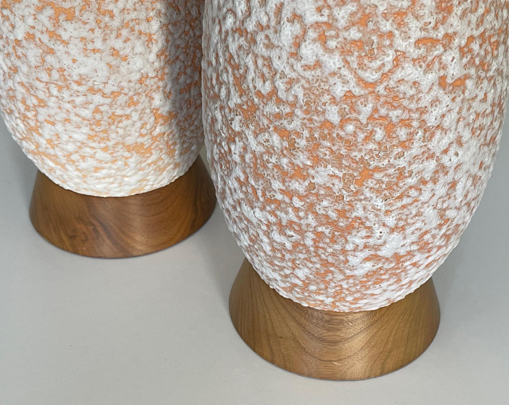 Each tall bottle-form lamp with a textured peach and white glaze all over a walnut base.