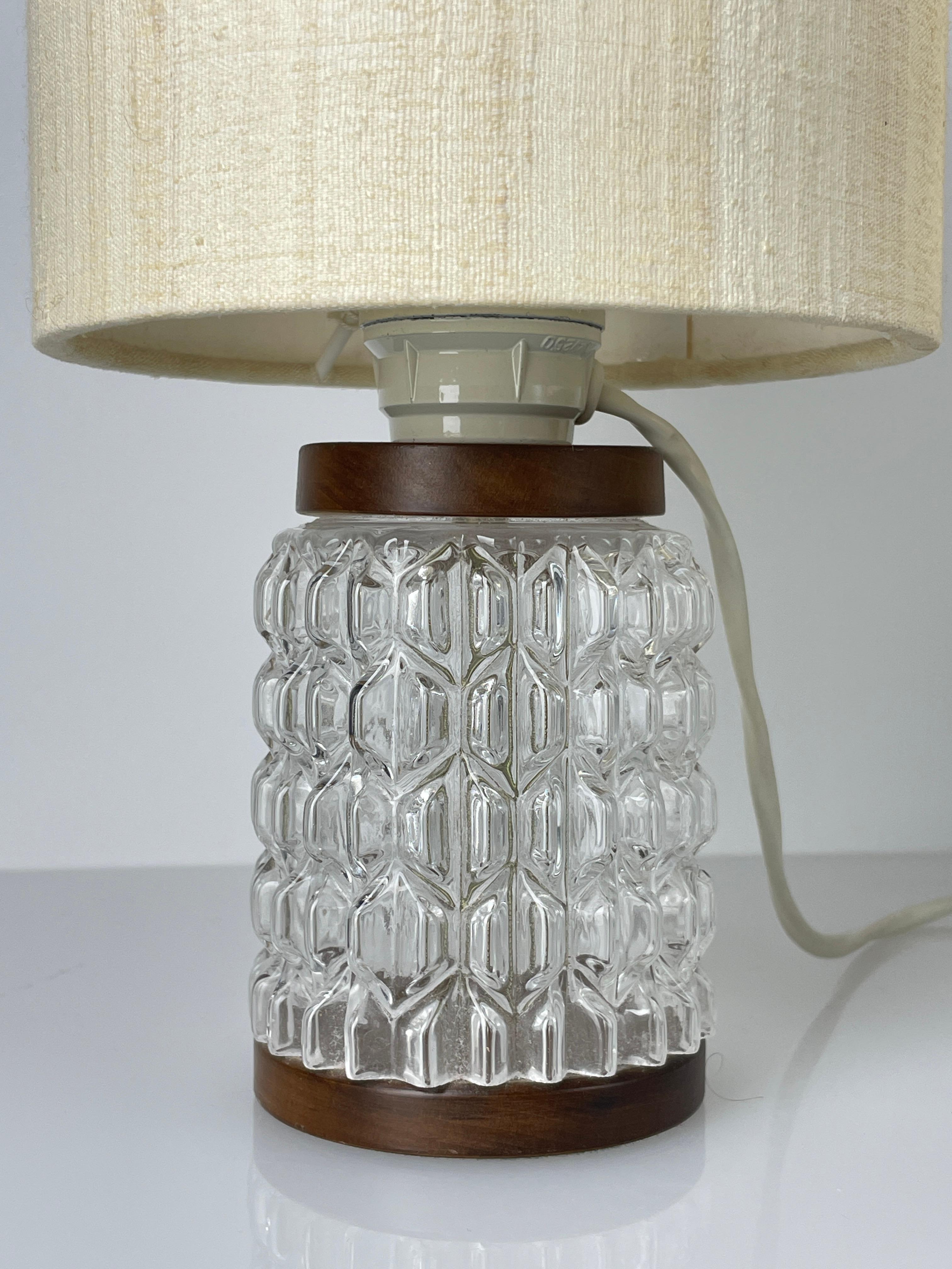 Magnifique paire de lampes de chevet des années 1960, modèle FW1, avec un abat-jour synthétique monté sur une base en verre bulle transparent avec des détails en noyer. Interrupteur marche/arrêt à câble avec prise murale suisse. La teinte crème