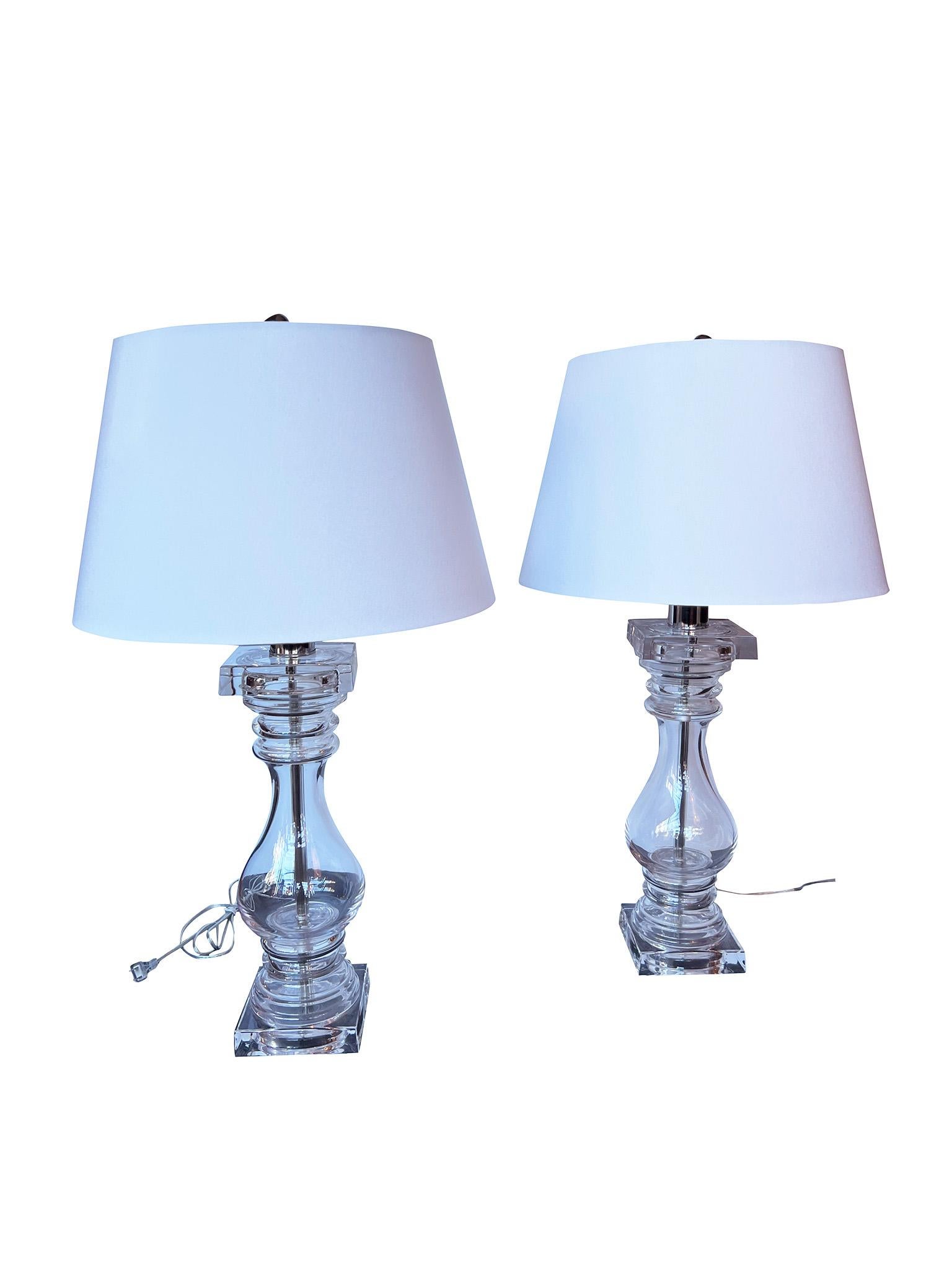 Lovely pair of 1970s baluster shaped table lamps crafted by Chapman Glass. Characterized with mirrored thick square bases and tops, the clear glass is accented by original chrome fittings. One of the sockets has a sticker that reads 