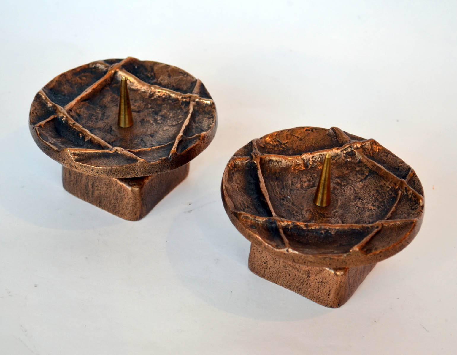 Bronze cast pair of round low candle holders on square feet with geometric pattern on the surface, suitable for 4-5 cm wide candles.