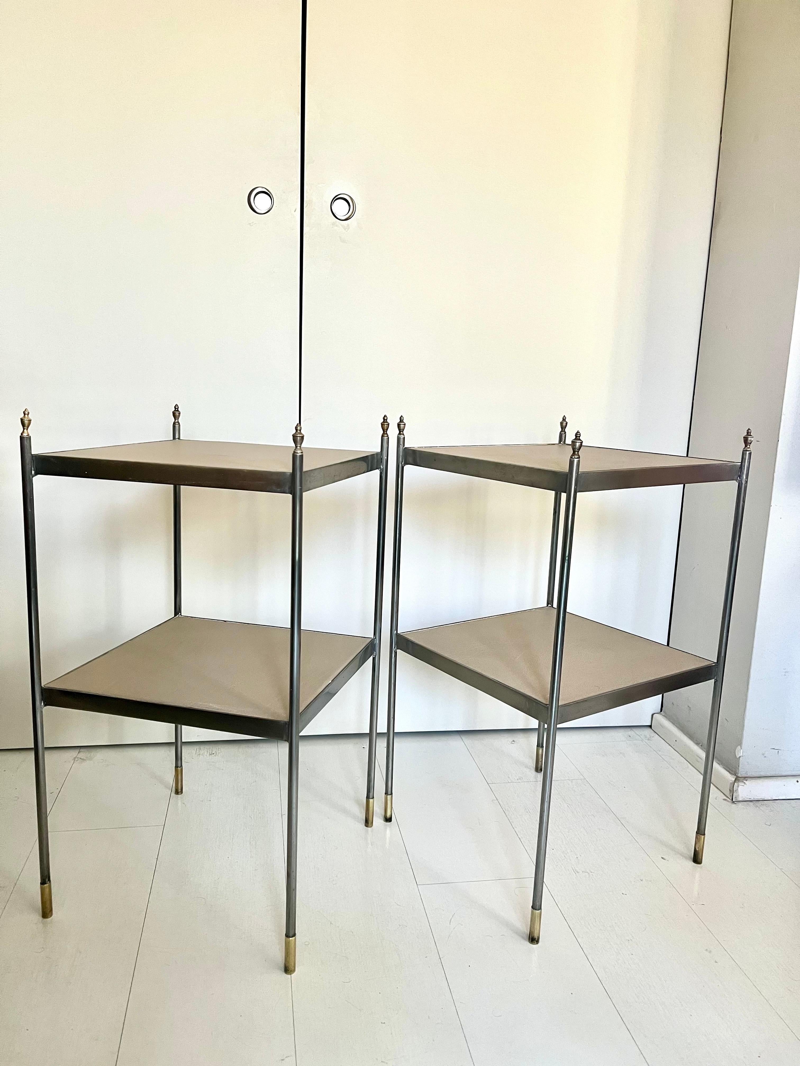 A pair of Maison Jansen-style side tables. Chrome-plated metal frame with slim, clean lines typical of the Mid-Century Modern or Hollywood Regency style, brass details on both the underside of the legs and the finials that top the tables, with two