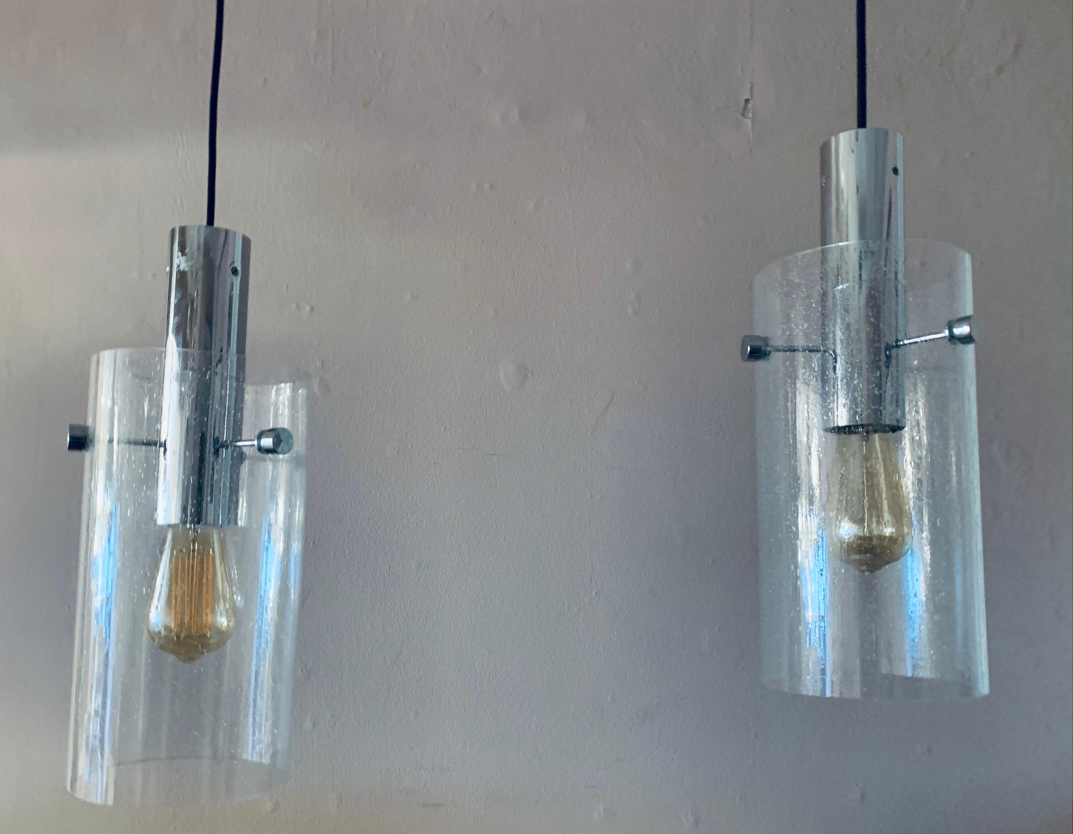 Paire de suspensions cylindriques en verre clair bullé Glashütte Limburg des années 1970, suspendues à des ferrures chromées et à un flexible noir réglable. L'abat-jour en verre bullé est suspendu à un cylindre chromé par trois tiges de support