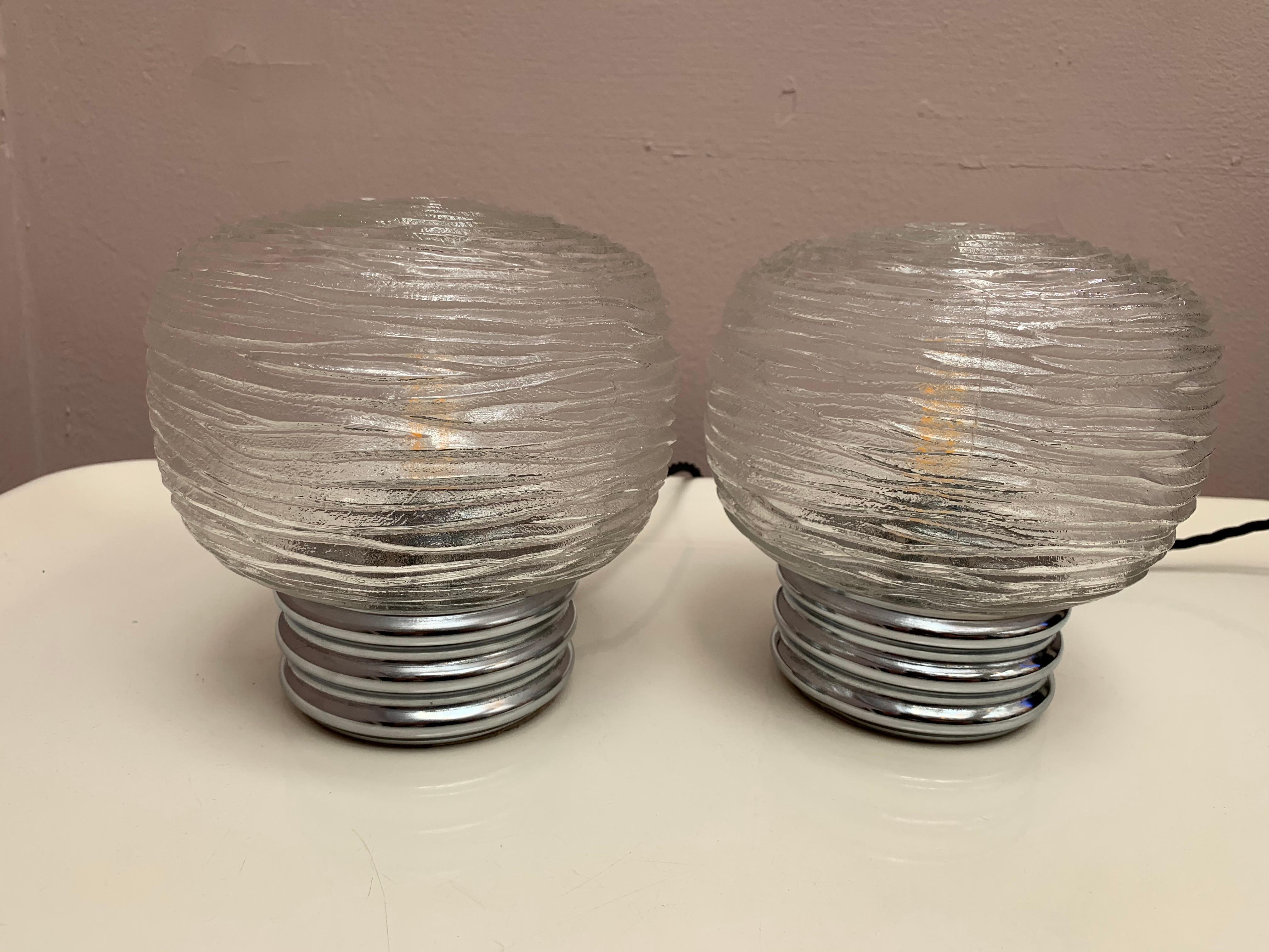 An unusual pair of chrome and glass table lamps each featuring an interesting swirled rose design around its surface. Manufactured by Hillebrand, Germany in the 1970s. The glass shade sits on a circular chrome base each with a felt bottom. An