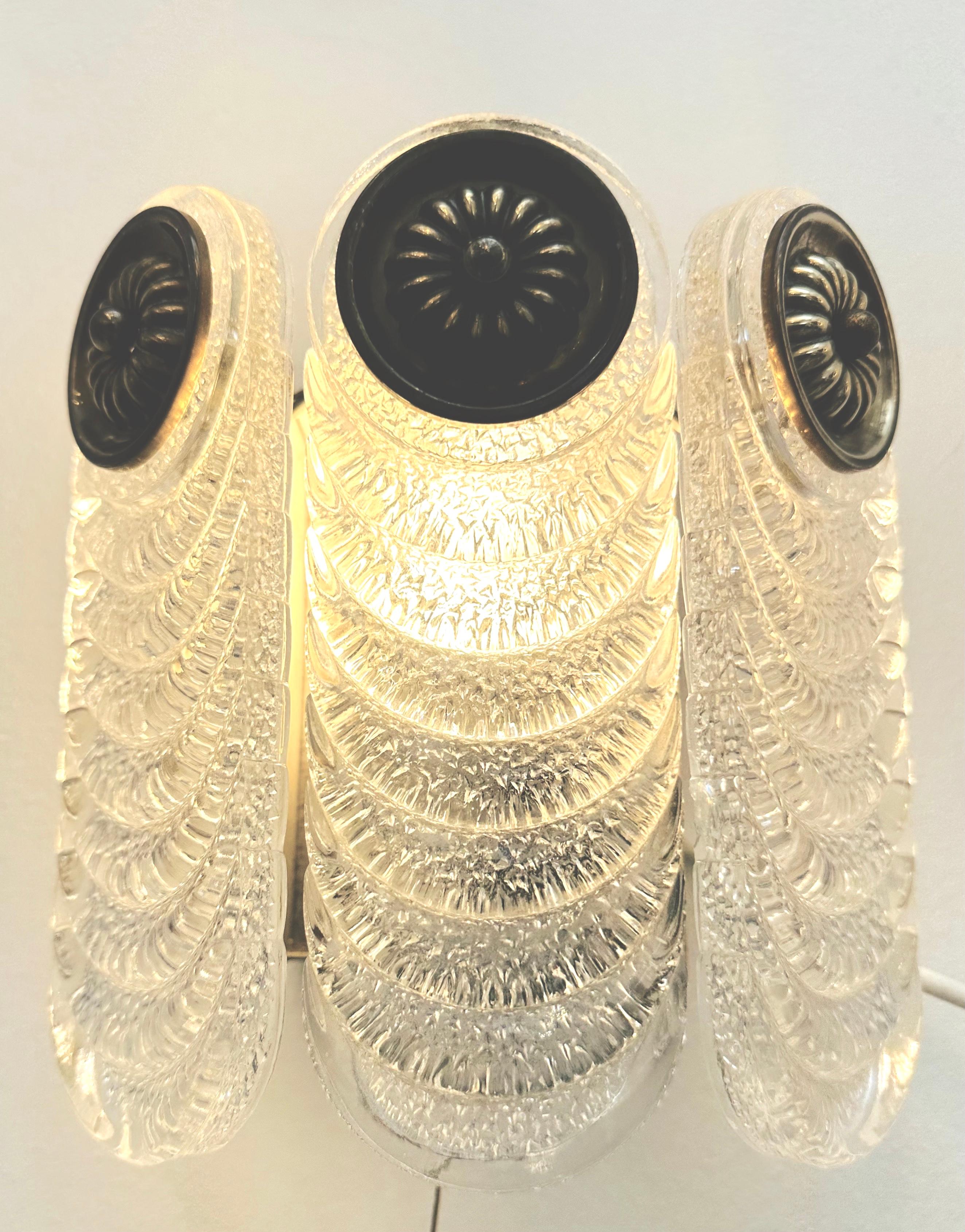 Coppia di applique in vetro di Murano e ottone Kaiser Leuchten degli anni '70. Il portalampada ha l'interno in metallo bianco e la parte superiore in ottone invecchiato, da cui pendono i tre steli in vetro di Murano con design a increspature,
