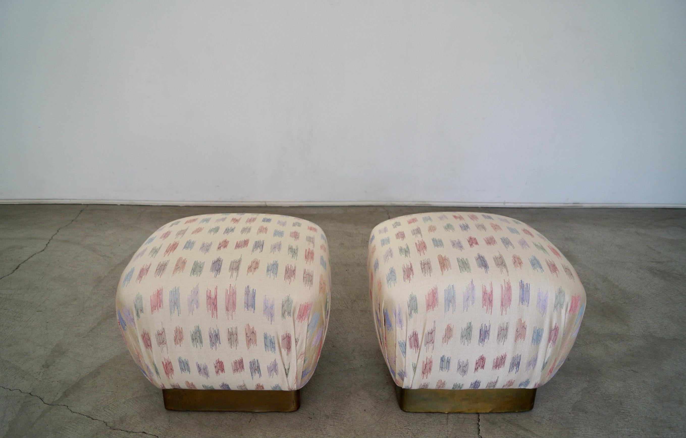 Pair of vintage Hollywood Regency ottoman poufs for sale. Manufactured in the 1970's by Marge Carson, and have been reupholstered in a beautiful designer fabric. They have a brass plinth base, and came out beautifully. The brass has aged