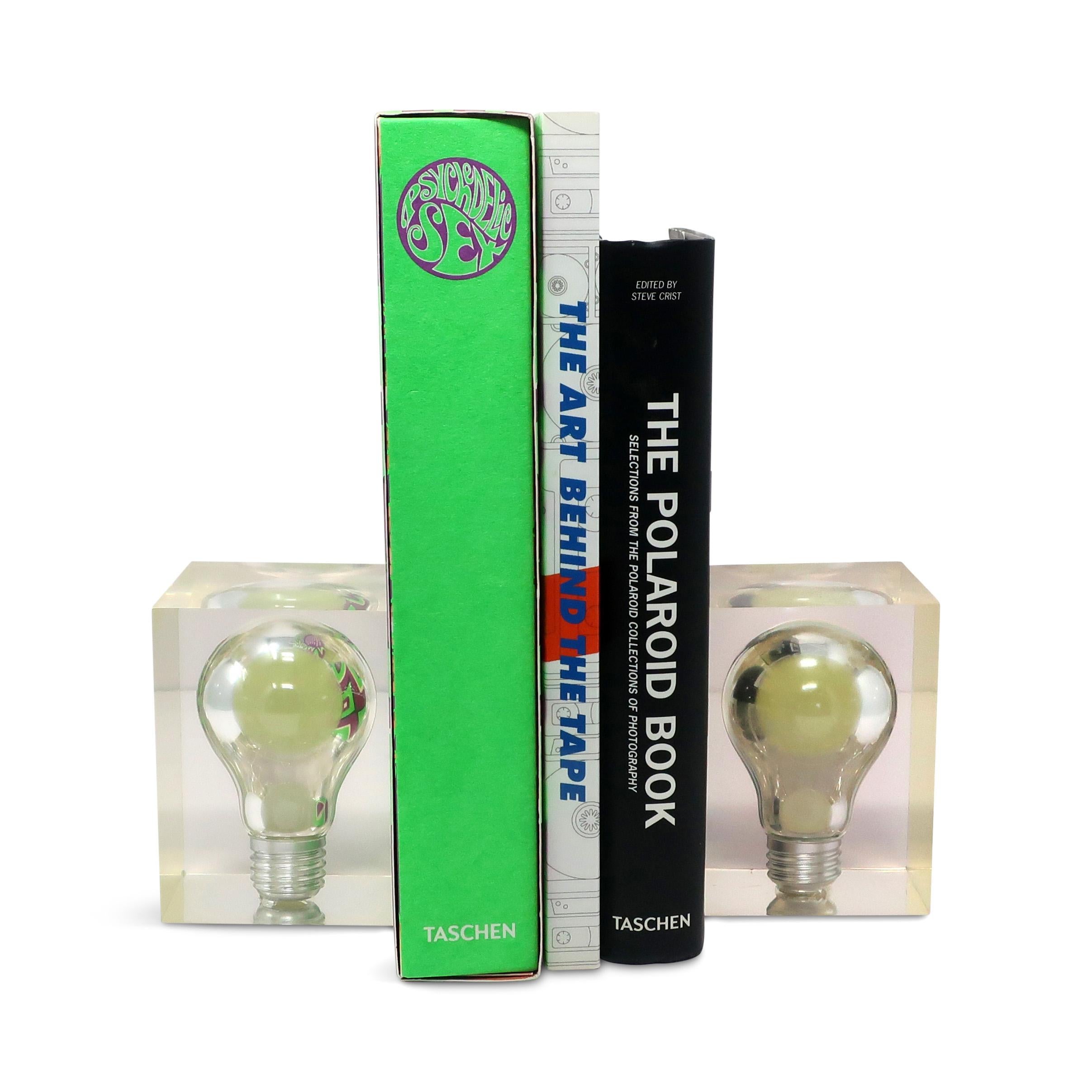 A striking and whimsical pair of bookends with lightbulbs filled with a phosphorescent (glow in the dark) substance suspended in a lucite cube.  The pair was designed by Pierre Giraudon, an artist and designer known for suspending items in lucite in