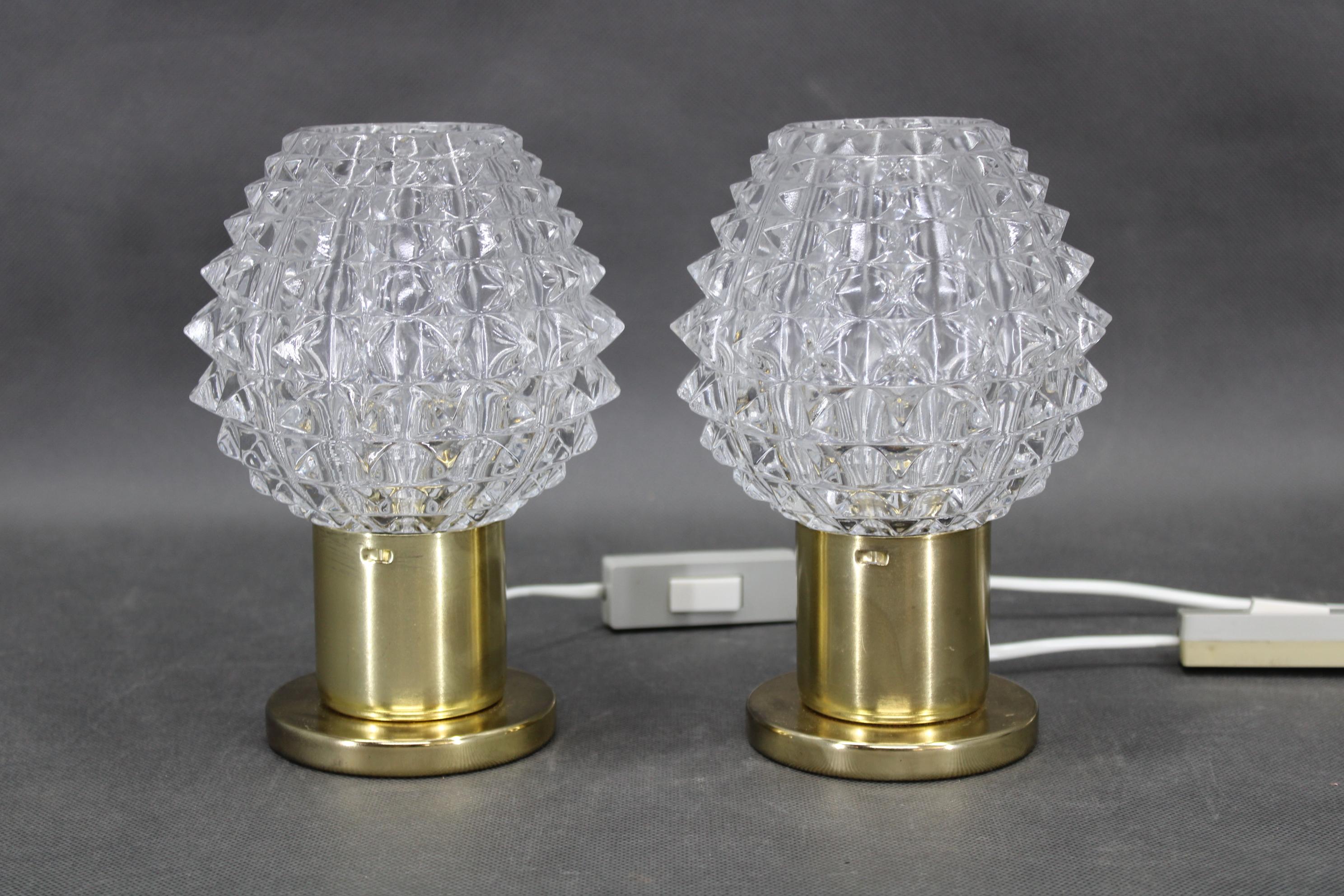 A vintage pair of mid-century table lamps produced in the 1970s in Kamenický Šenov, a renowned Czech glassmaking center. Each lamp features a sculptural prismatic glass shade with strong geometric texture, paired with a brass-finish metal base that