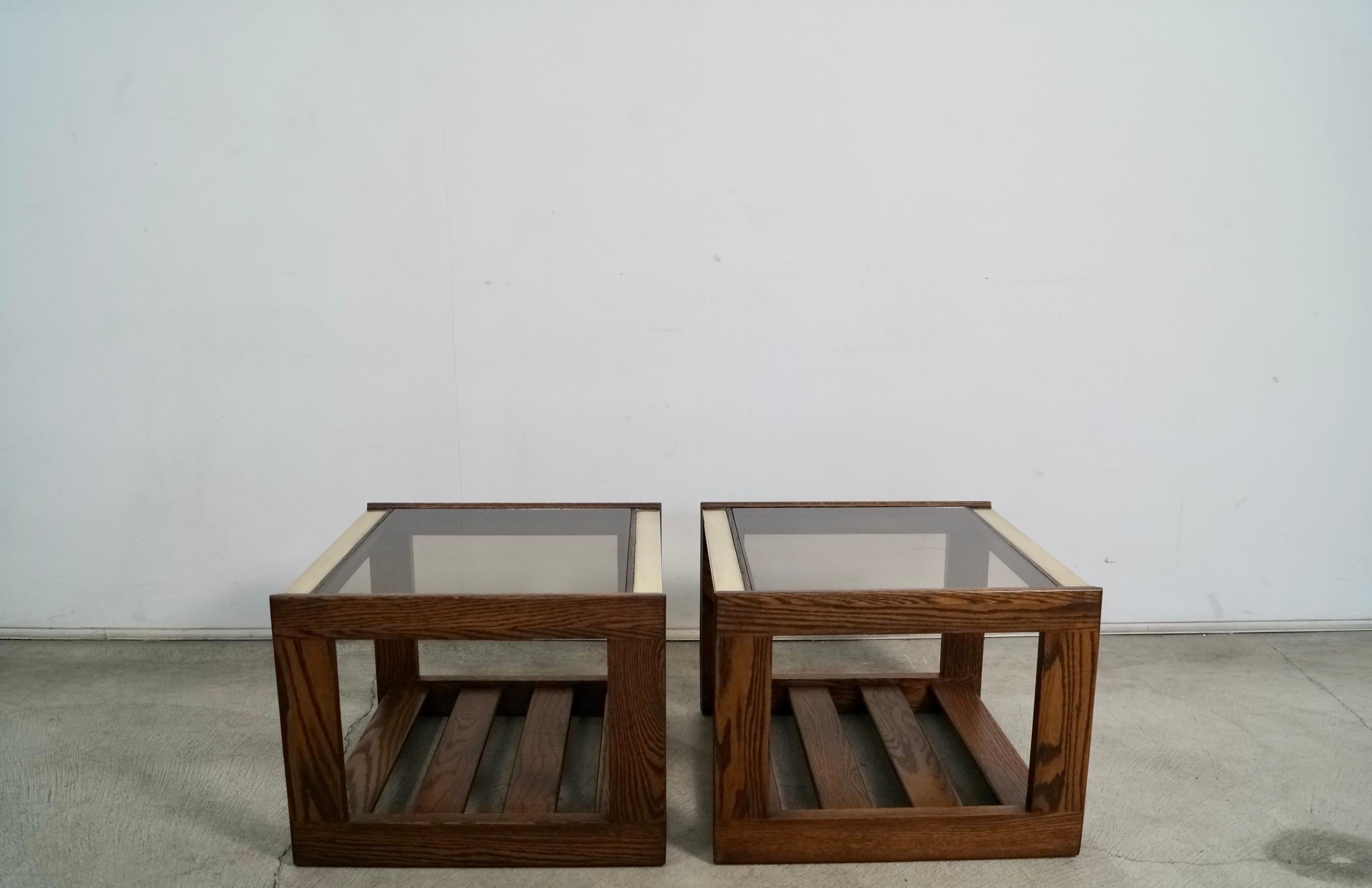 Pair of vintage Midcentury Modern side tables for sale. They were manufactured in the 1970's, and have been refinished in walnut. They have an oak frame with a smoked glass insert and brass accents on the top. They have solid oak slats as a shelf