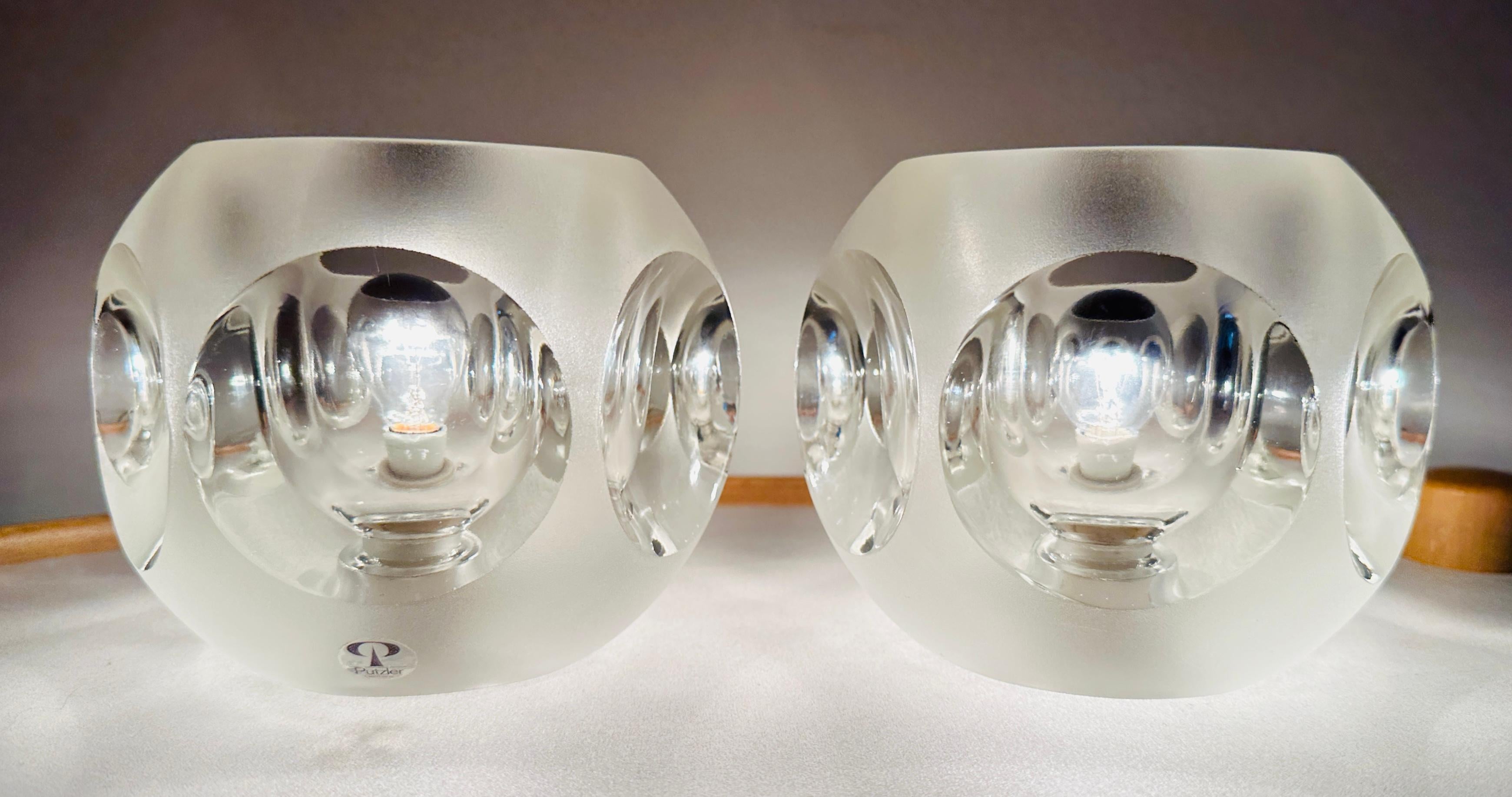 This pair of 1970s German table lamps by Peill and Putzler features a circular design made of frosted and clear glass. Six concave indentations on each lamp beautifully magnify and reflect the light.

The lamps have been inspected by an electrician
