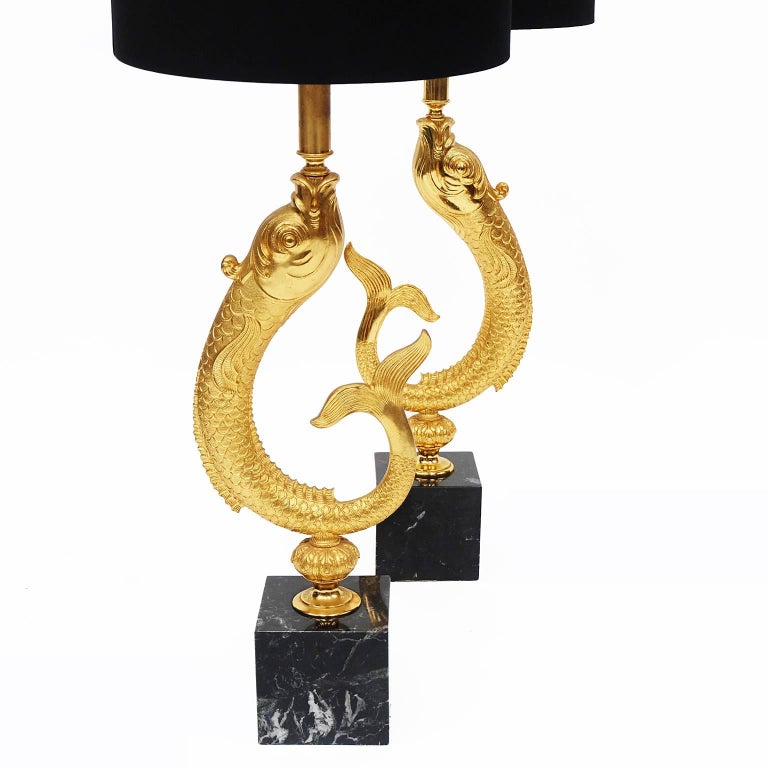 Pair of large 1970s table lamps designed and manufactured in France.

Decorative gold-plated fish design with black drum lampshades.

Portoro marble cube plinths.

Measures: With shade H 92cm x W 35.5cm x D 35.5cm.
Without shade H 74cm x W