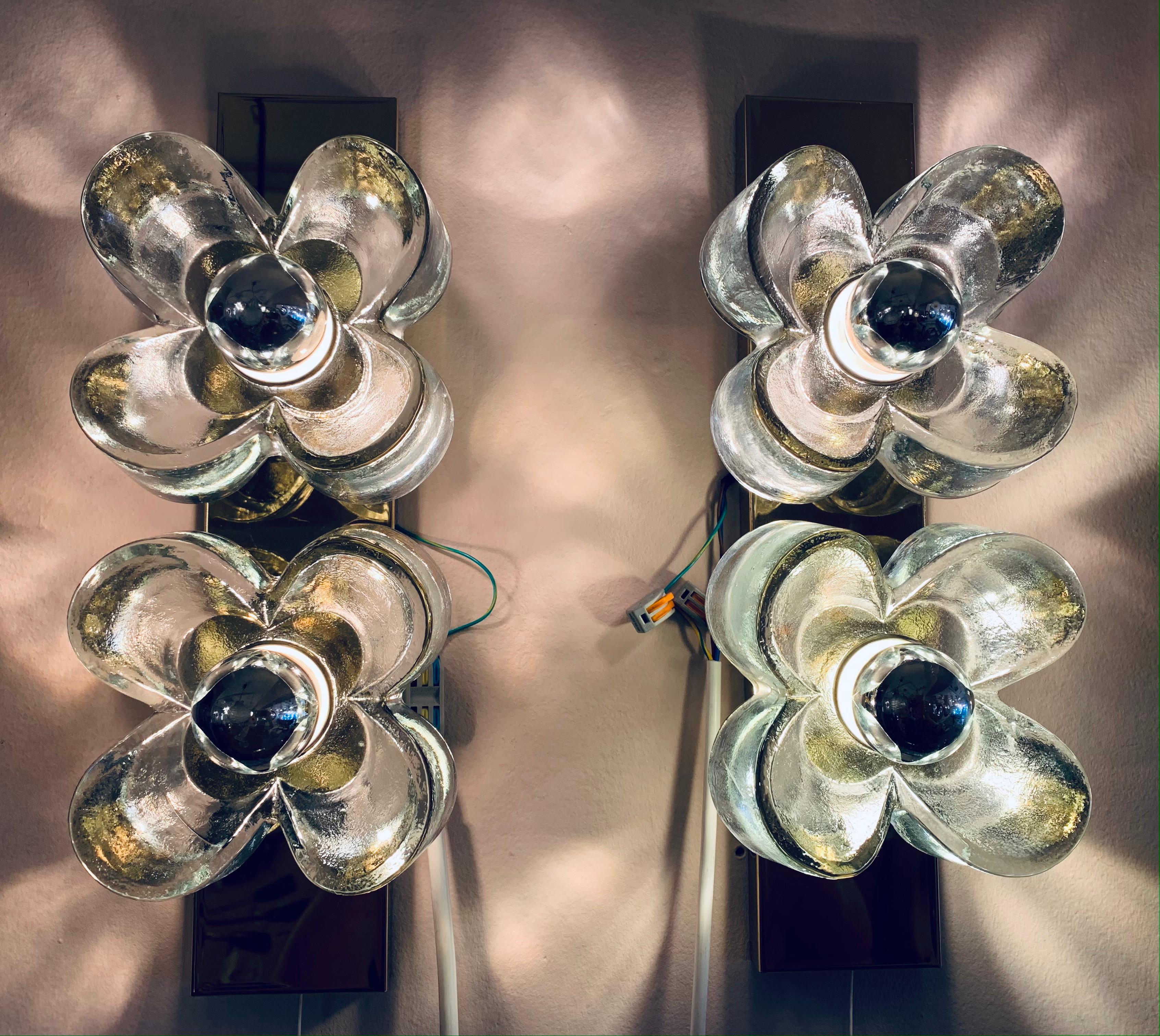 A striking and unusual pair of flower wall sconces or wall lights designed by Simon and Schelle for Sische Lighting during the 1970s in Germany. The two Murano glass four petal flowers are secured onto the brass base with screwable chrome rings. The