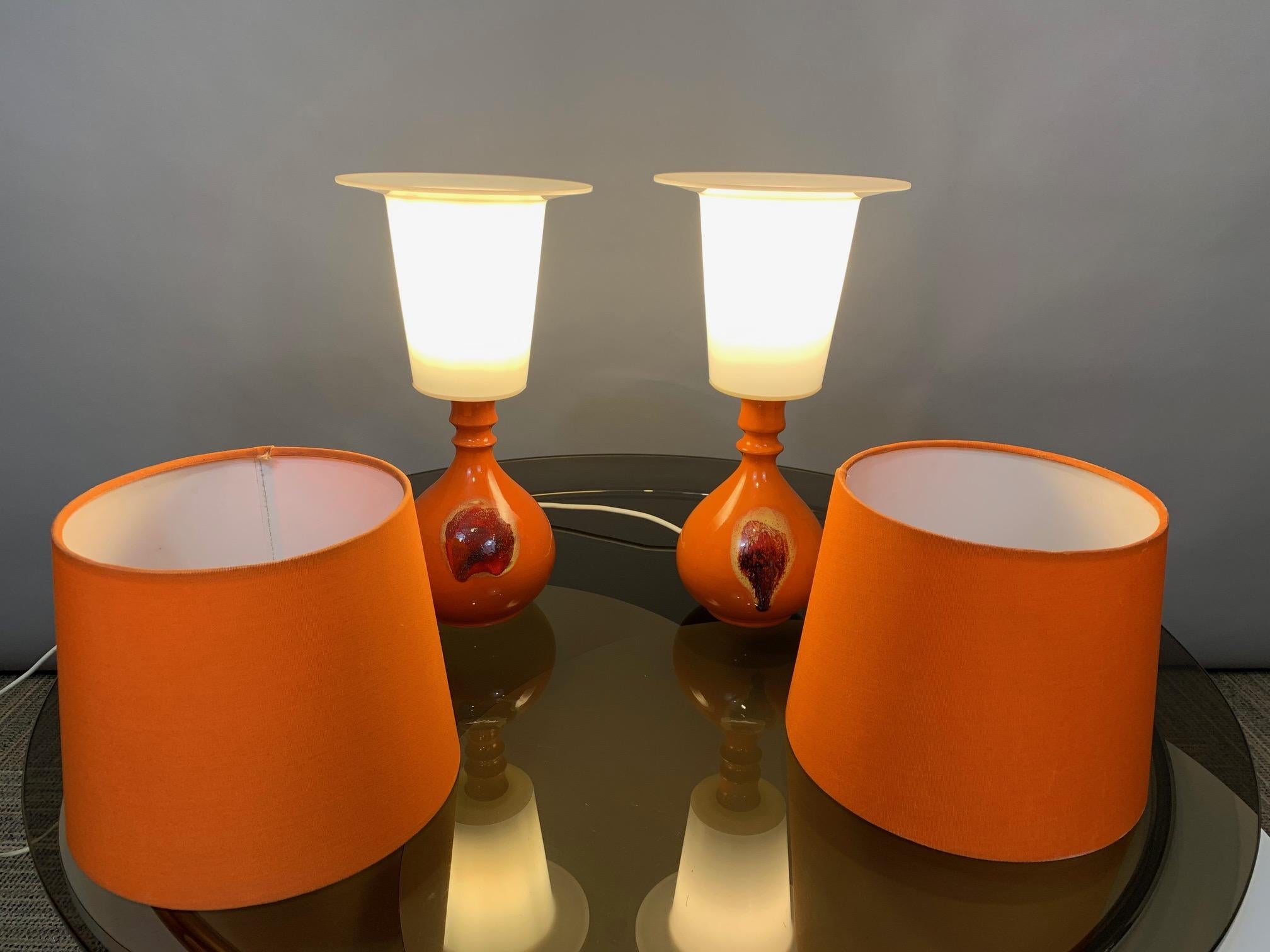A pair of small 1970s German Rosenthal 'Studio Line' orange glazed ceramic lamps including their original shades with white plastic interiors. Designed by Bjørn Wiinblad for Rosenthal • Studio Line in Germany. The lamps are stamped on the hole where
