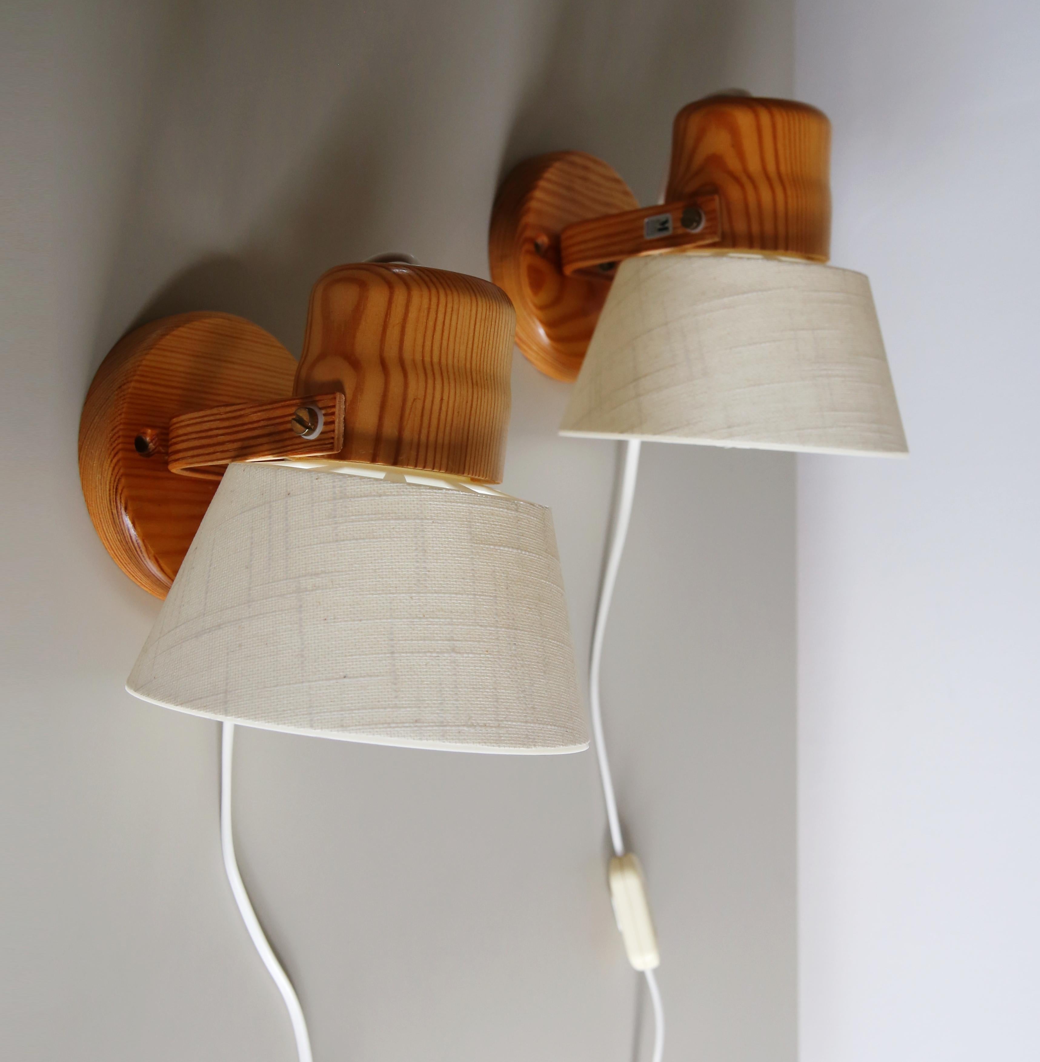 Lovely pair of 1970s Swedish pine wall lamps by Markslojd. 
With a textured cream fabric shades that have a rigid plastic inner lining, the lamp heads can be both rotated and tilted up and down.

I will send these with brass wall screws that match