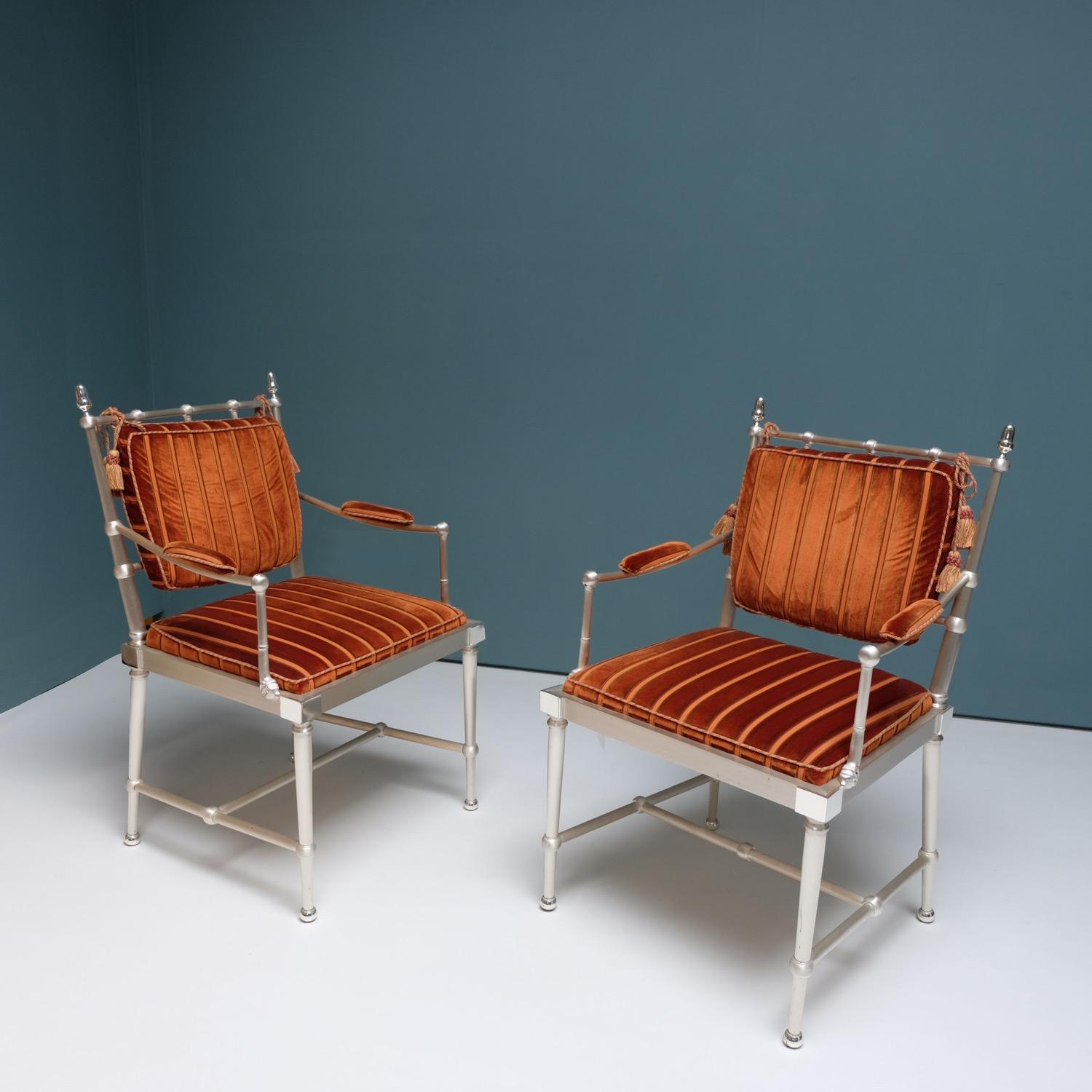 A stunning and unique pair of 1980s brushed and polished nickel armchairs. The armchairs have been attributed to Christian Dior. The cushions have been recovered in a burnt orange deep velvet fabric with contrasting orange stripes. A pair of tassels