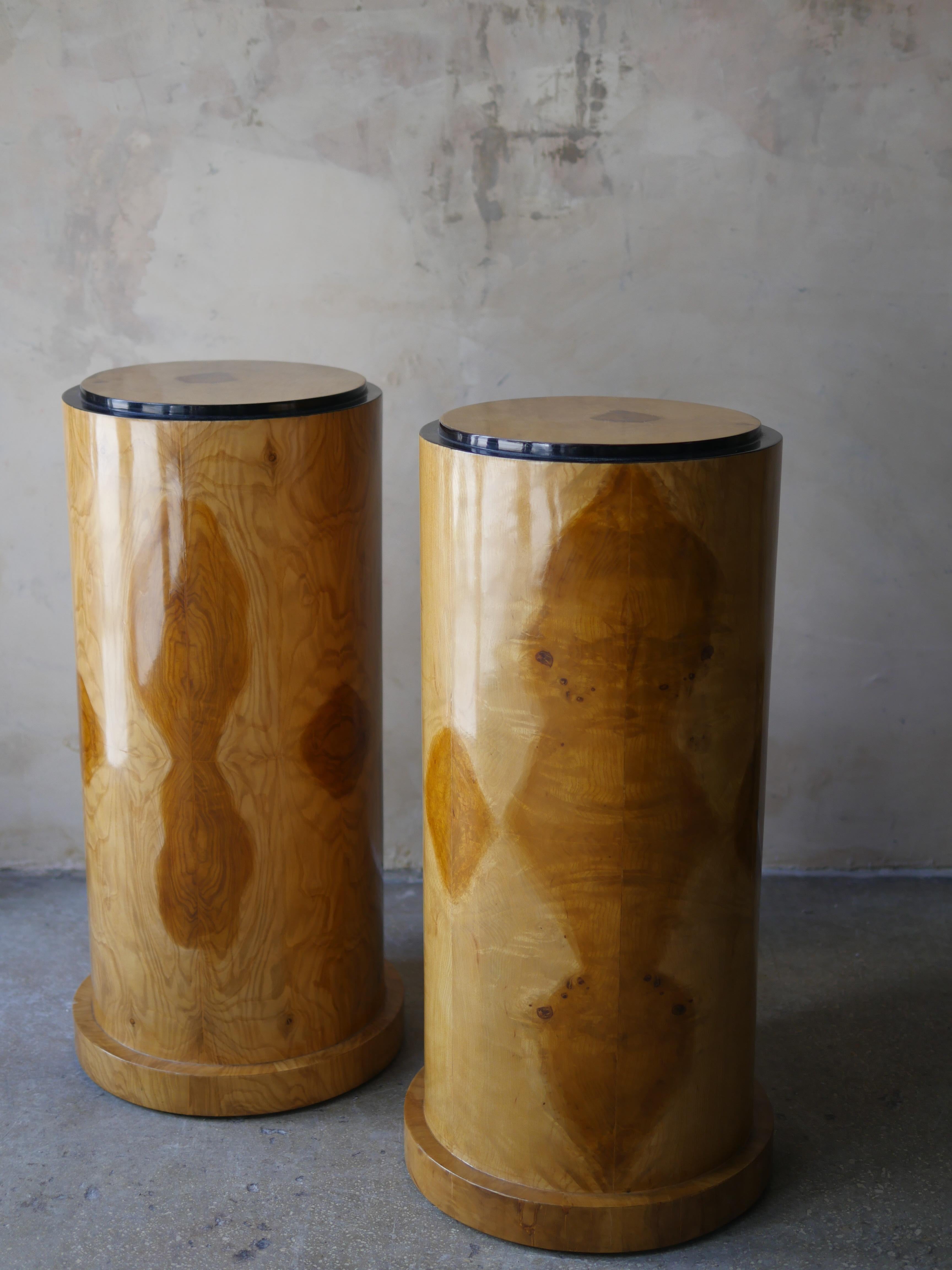 A pair of 1980s Italian, cylindrical pedestals featuring richly figured burl wood veneers and black lacquered trim tops. These beautiful pedestals feature an organic symmetry of burl grain, wrapped around a sleek, cylindrical form. The glossy black