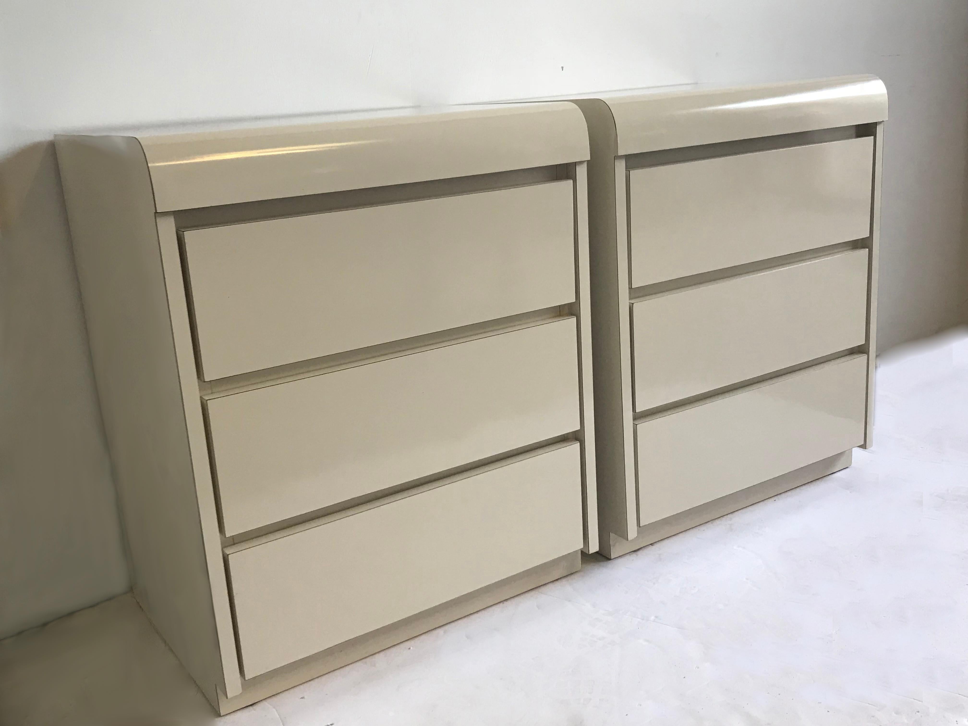 A pair of off-white lacquer laminate formica nightstands.
These glossy stands have 3 drawers and a curved front edge.