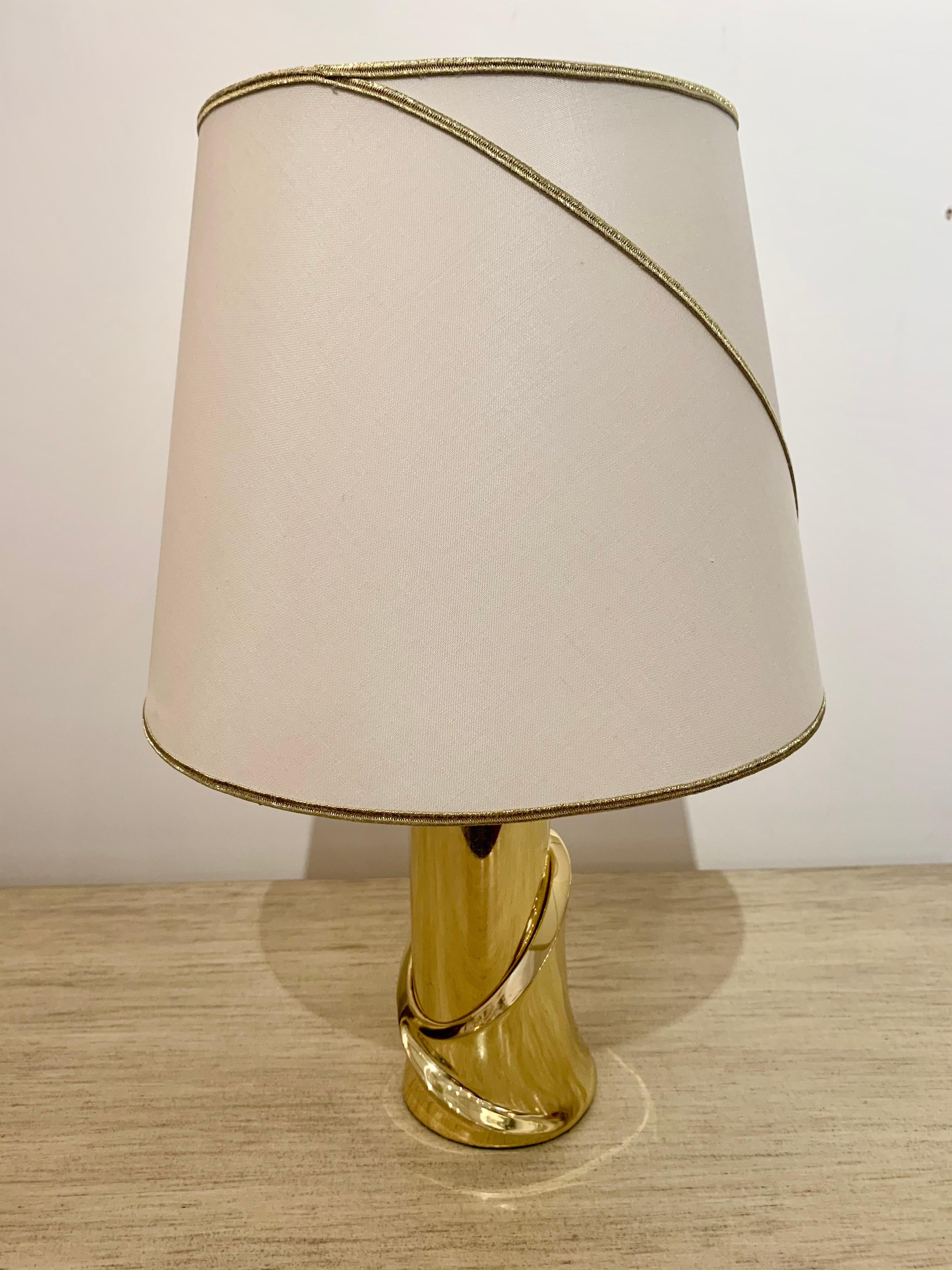 A pair of luxurious 1980s sculptural polished bronze table lamps with the original matching shades. The shades have been newly recovered and the gold piping matches the swooping lines design of the bases. Newly rewired. Made by coveted Italian