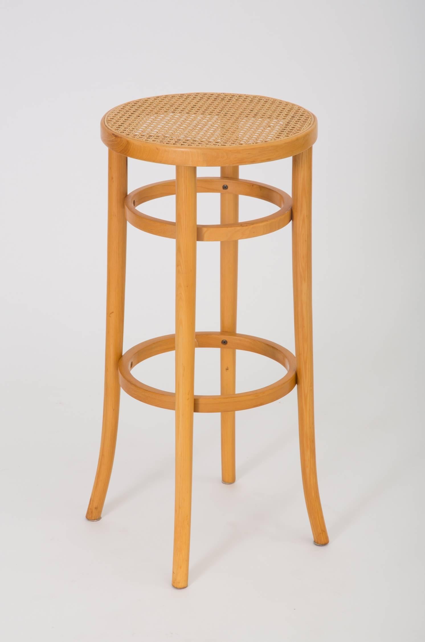 A pair of 1980s American-made Thonet Industries round bar-height stools, manufactured in Thonet’s signature bent birchwood with woven cane seats. Each stool has four rounded saber legs and two support rings below the seat and at foot level. Both