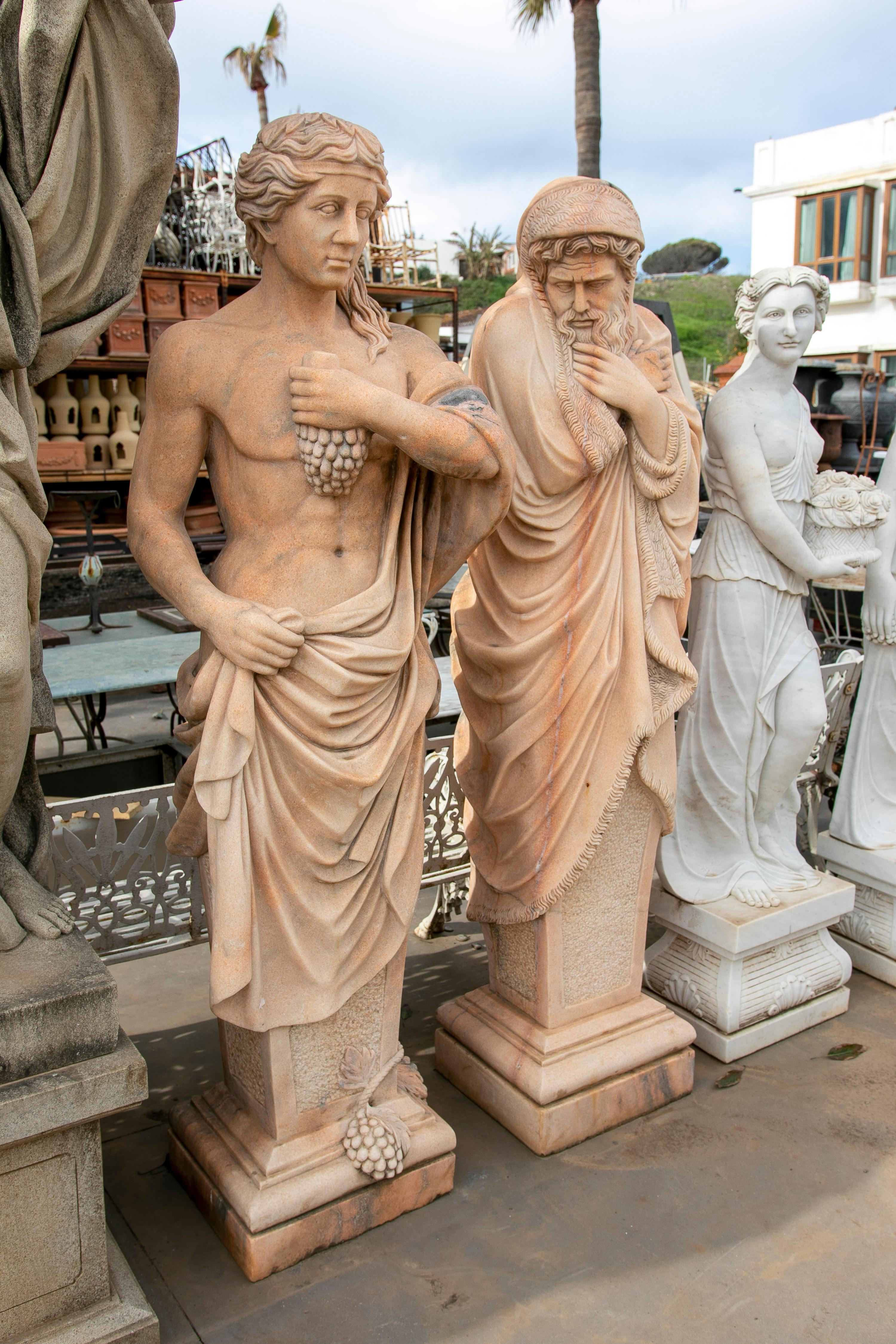 Pair of 1990s hand carved Rosetta pink male sculptures, one holding grapes and representing autumn, the other covered by a blanket as a representation of winter.