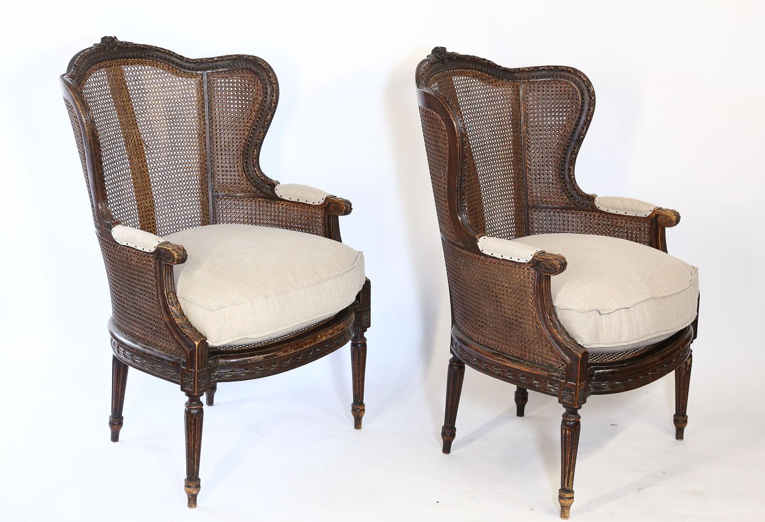 This pair of 19th century cane backed bergère chairs are hand carved and caned. Featuring a newly upholstered Belgian linen seat cushion. This style never goes out of fashion and they are the most comfortable thing to sit in.