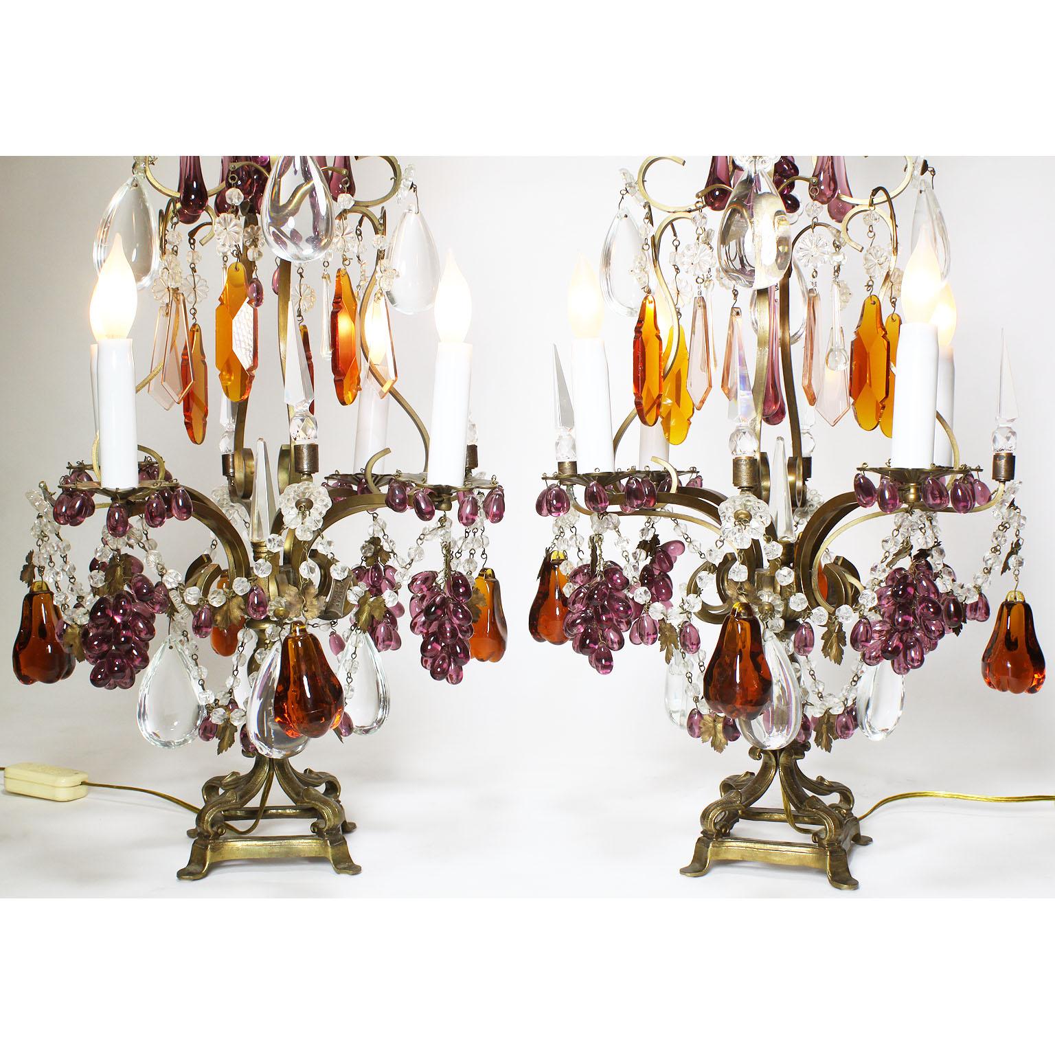 A pair of Italian 19th-20th century Florentine cut-clear and color glass four-lights girandoles table lamps. The scrolled bronze frame with four scrolled candle-arms, surmounted with cut-glass tear-drops, floral design cut-glass petals, amethyst