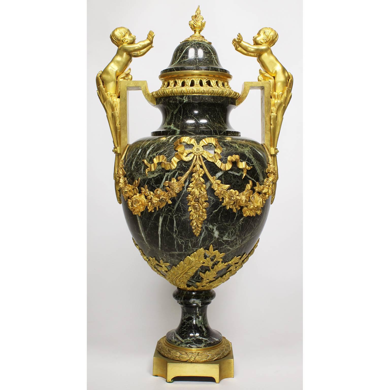 Paire d'urnes en bronze doré (Ormolu) et en marbre Vert Maurin (marbre vert veiné), de style Louis XVI, du 19e au 20e siècle. Le couvercle amovible en forme de dôme est centré par un fleuron en forme de flambeau. Le corps ovoïde est flanqué d'une