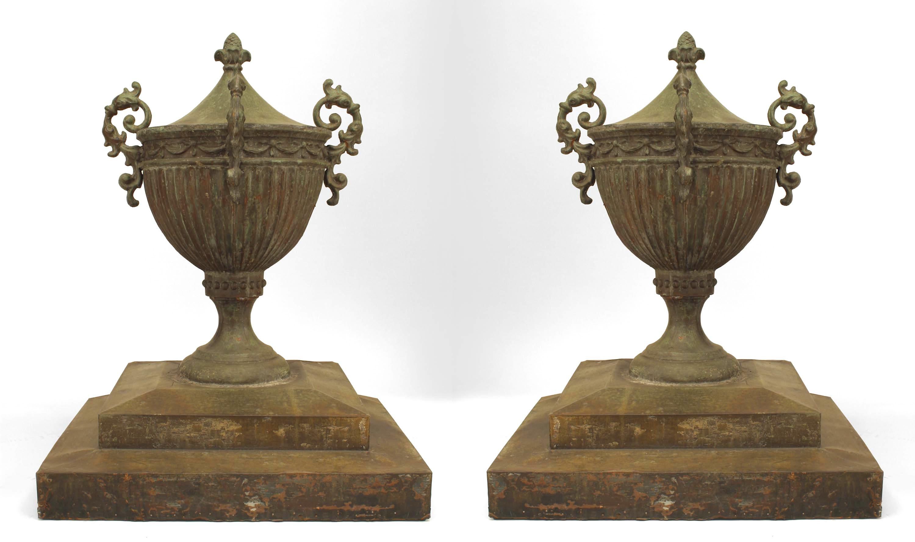 Pair of English Adam style (18/19th Cent) copper outdoor urns with floral top finial on square base.
