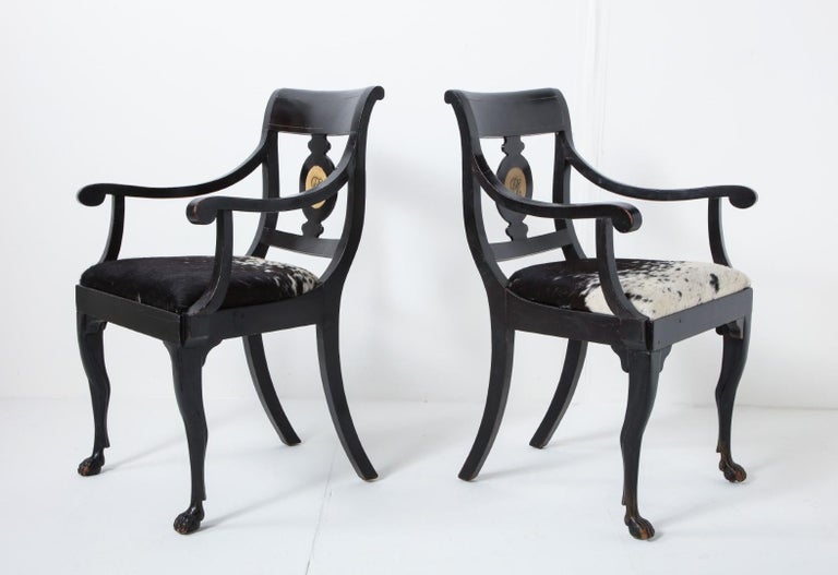A pair of 19th century English Regency ebonized armchairs with hand painted monogram. Natural pony hide seats in black and white.

Measures: Arm height 25
