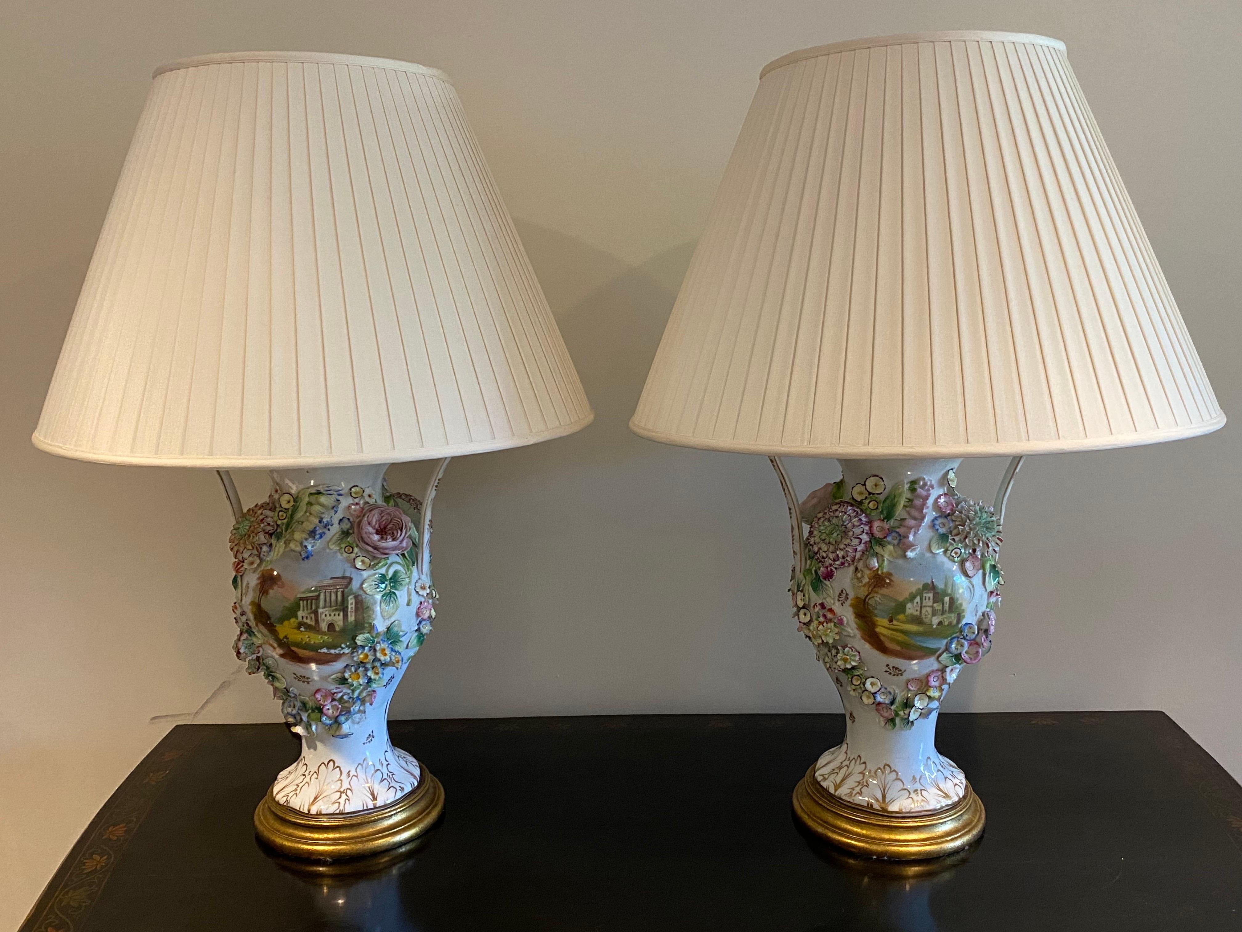 Pair of 19th C. English Coalport Porcelain Two Arm Vases Converted to Lamps.
Two arm glazed porcelain vases elaborately decorated with delicate porcelain flowers. A rural landscape scene hand painted in the center on either side of vase. Later