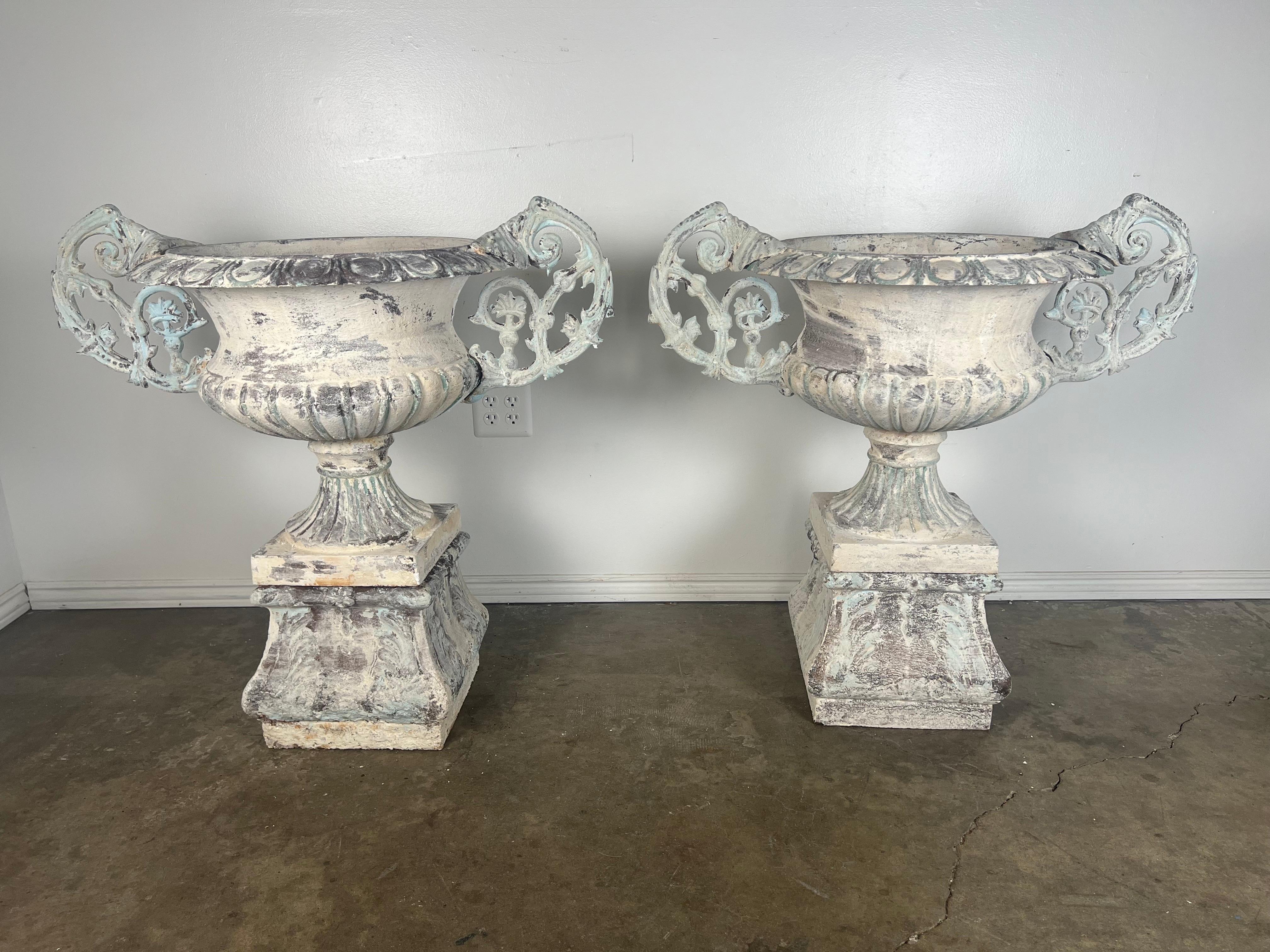 A pair of 19th century French cast iron painted garden urn planters, with weathered paint and rusted patina.   Nicely cast scrolled details on the double handles.