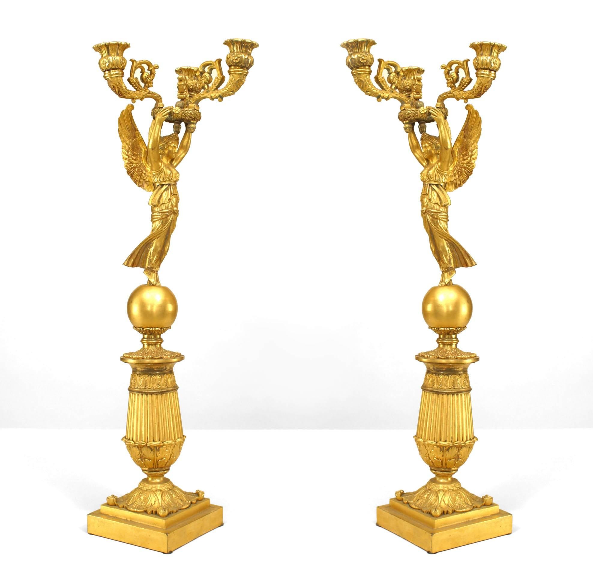 Pair of nineteenth century French Empire style bronze dore three arm candelabra, each featuring a classical winged victory or Nike figure positioned atop a tiered, architectural pedestal.