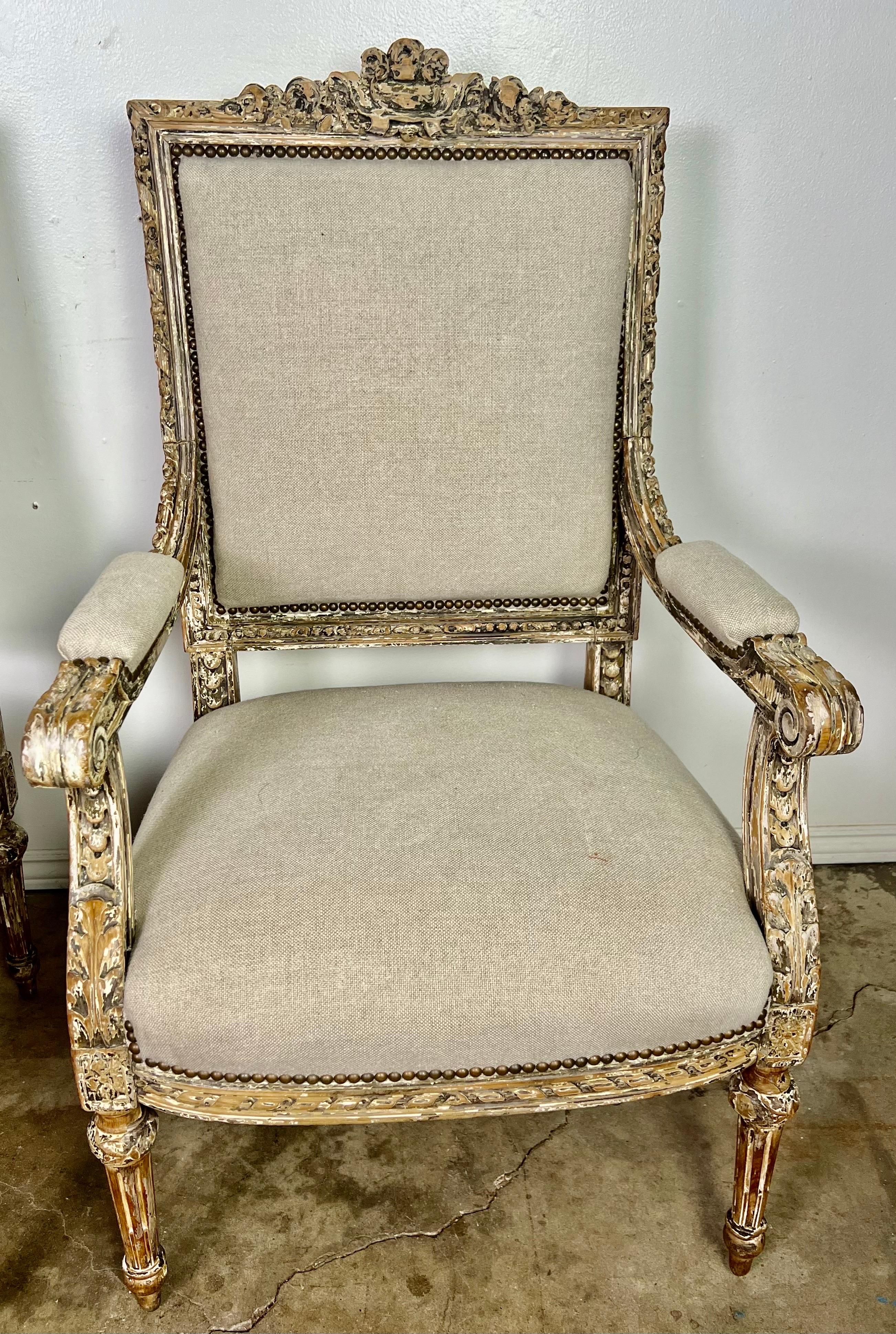 Pair of 19th C. French painted Louis XVI style armchairs.   The paint is beautifully worn depicting remnants of gray, brown & white colors throughout.  The natural color of the wood can be seen underneath the paint.  The armchairs are newly