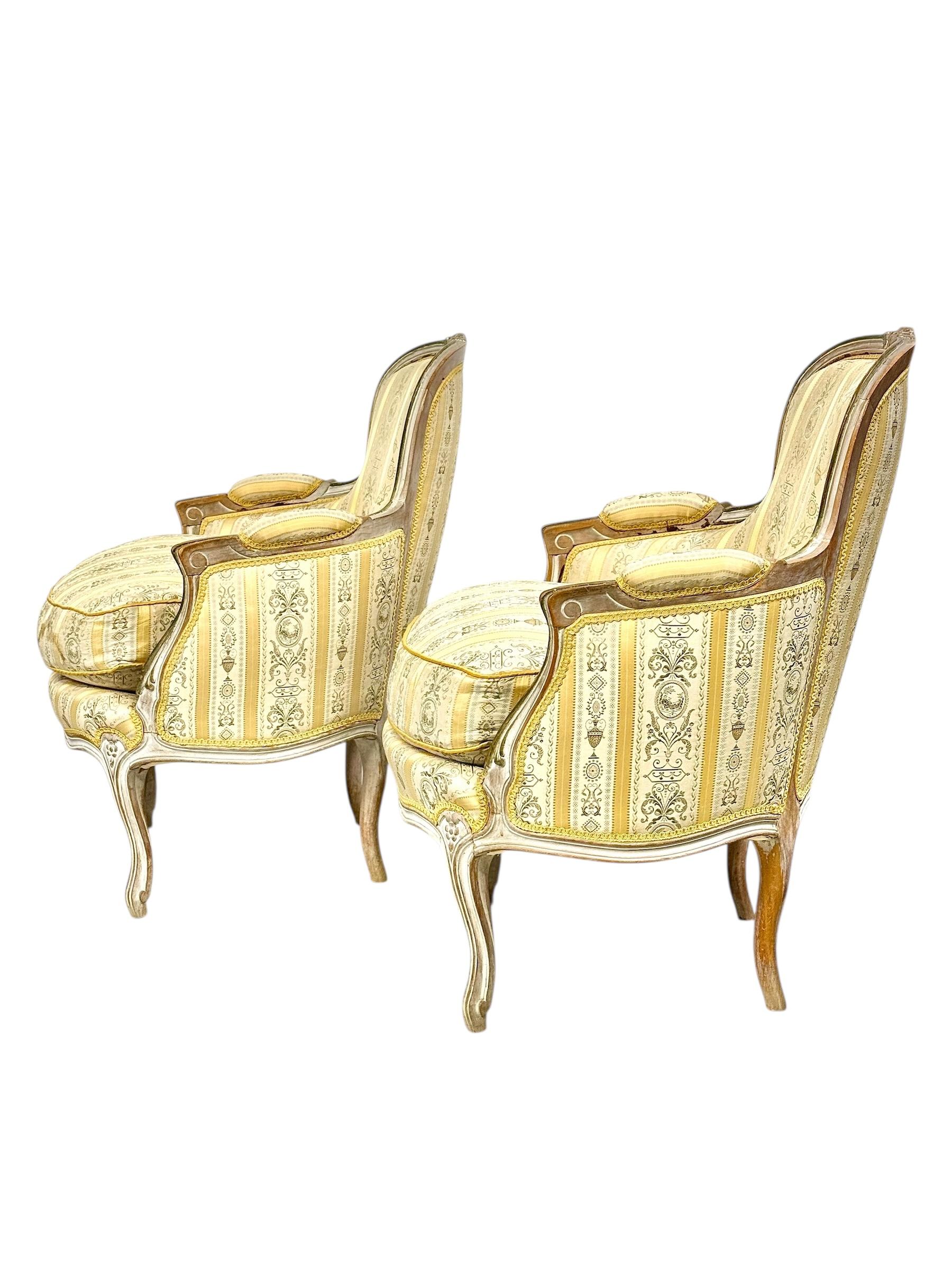 This elegant pair of French Louis XVI-style bergères exemplifies the timeless grace of neoclassical design. Dating from the late 19th century (circa 1880–1900), these generously proportioned armchairs feature intricately carved beechwood frames with