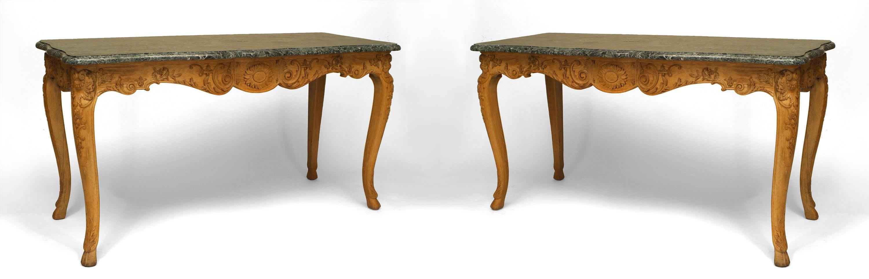 Pair of French Provincial Louis XV-style (19th Century) stripped oak console tables with serpentine green marble top above a sunflower carved apron on cabriole legs with hoof feet (priced as pair).   
  
