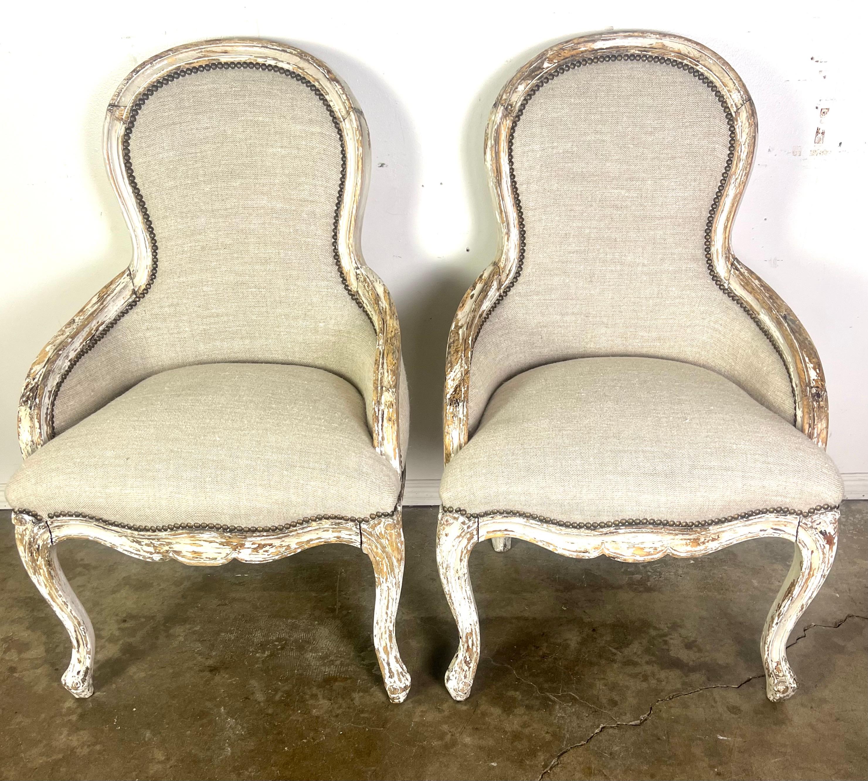 Coppia di sedie del XIX secolo dal design elegante e curvilineo tipico dei mobili in stile provinciale francese.  Sono caratterizzati da schienali alti e arrotondati che confluiscono senza soluzione di continuità nei braccioli, dando loro una forma