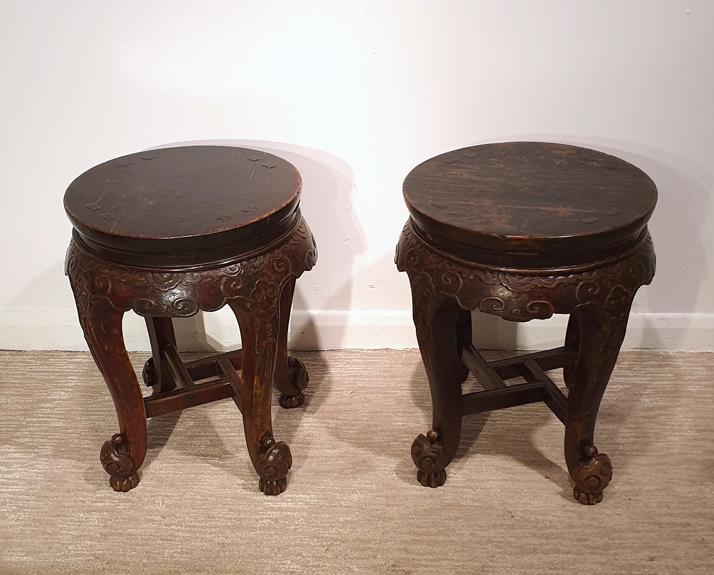 This lovely and decorative pair of 19th century Chinese hardwood stands feature a circular top and supported on 4 ornately carved cabriole legs joined together with a squared stretcher at the base. Each one measures 15 1/2 in - 39.4 cm in diameter