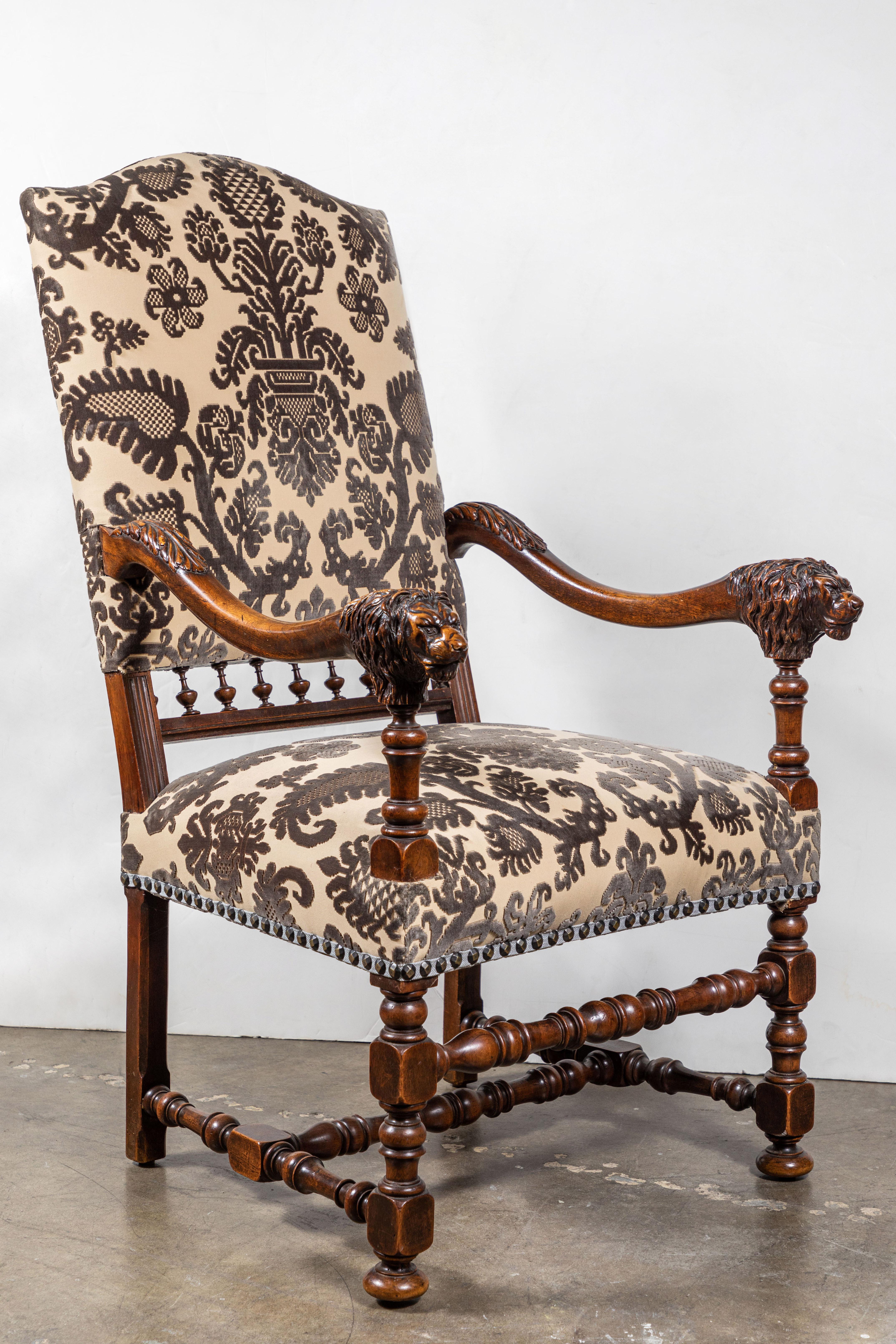 Beautifully carved, Italian, walnut chairs featuring serpentine arms terminating in lion's heads with flowing manes. Each atop turned legs and stretchers. Finished in a contemporary, chocolate and crème silk velvet fabric, and trimmed in