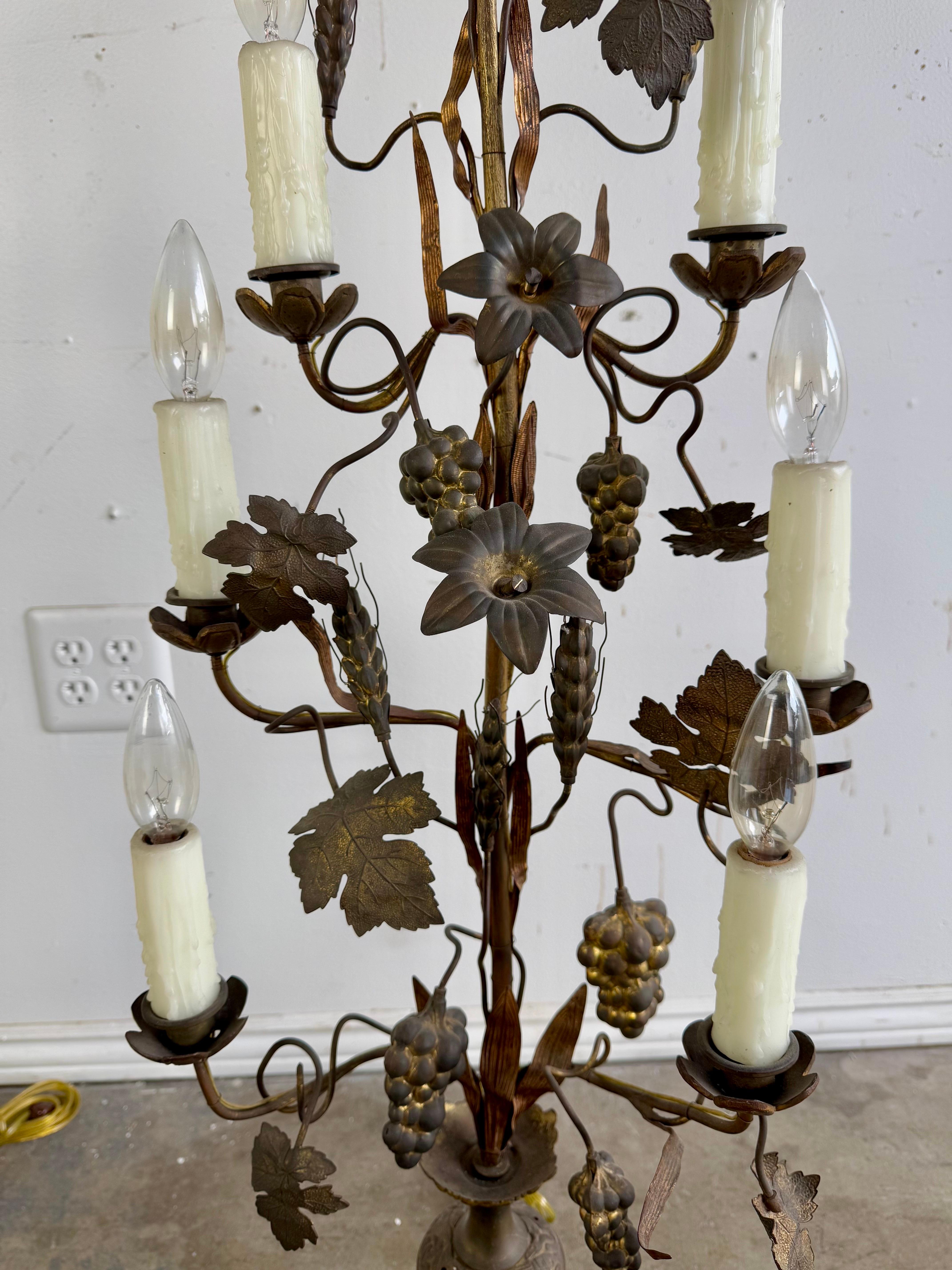 Pareja de candelabros italianos ornamentados.  Presentan una estructura metálica con intrincados motivos florales y de vides, incluidos racimos de uvas y hojas de vid.  Cada lámpara contiene varias bombillas de imitación de velas diseñadas para