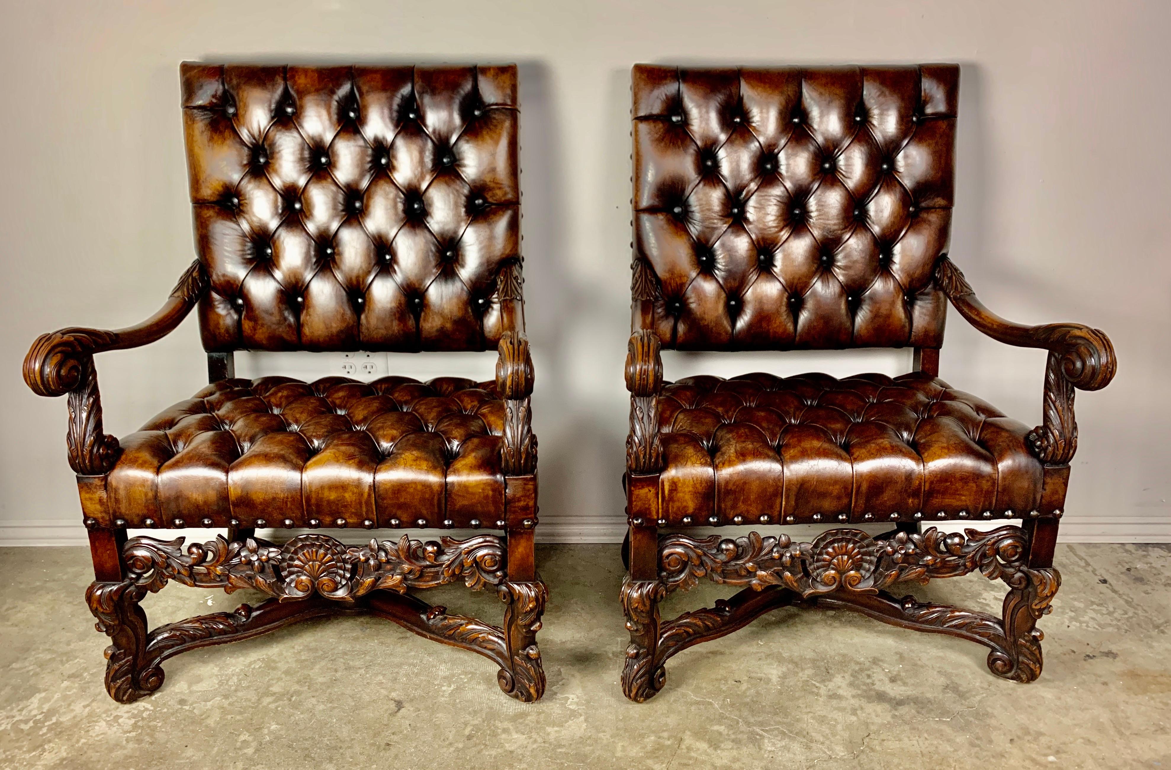 Pair of handsome 19th century walnut carved Italian armchairs upholstered in tufted leather with nailhead trim detail. Beautiful carved details throughout including a shell motif flanked by swirling acanthus leaves. The chairs stand on four carved