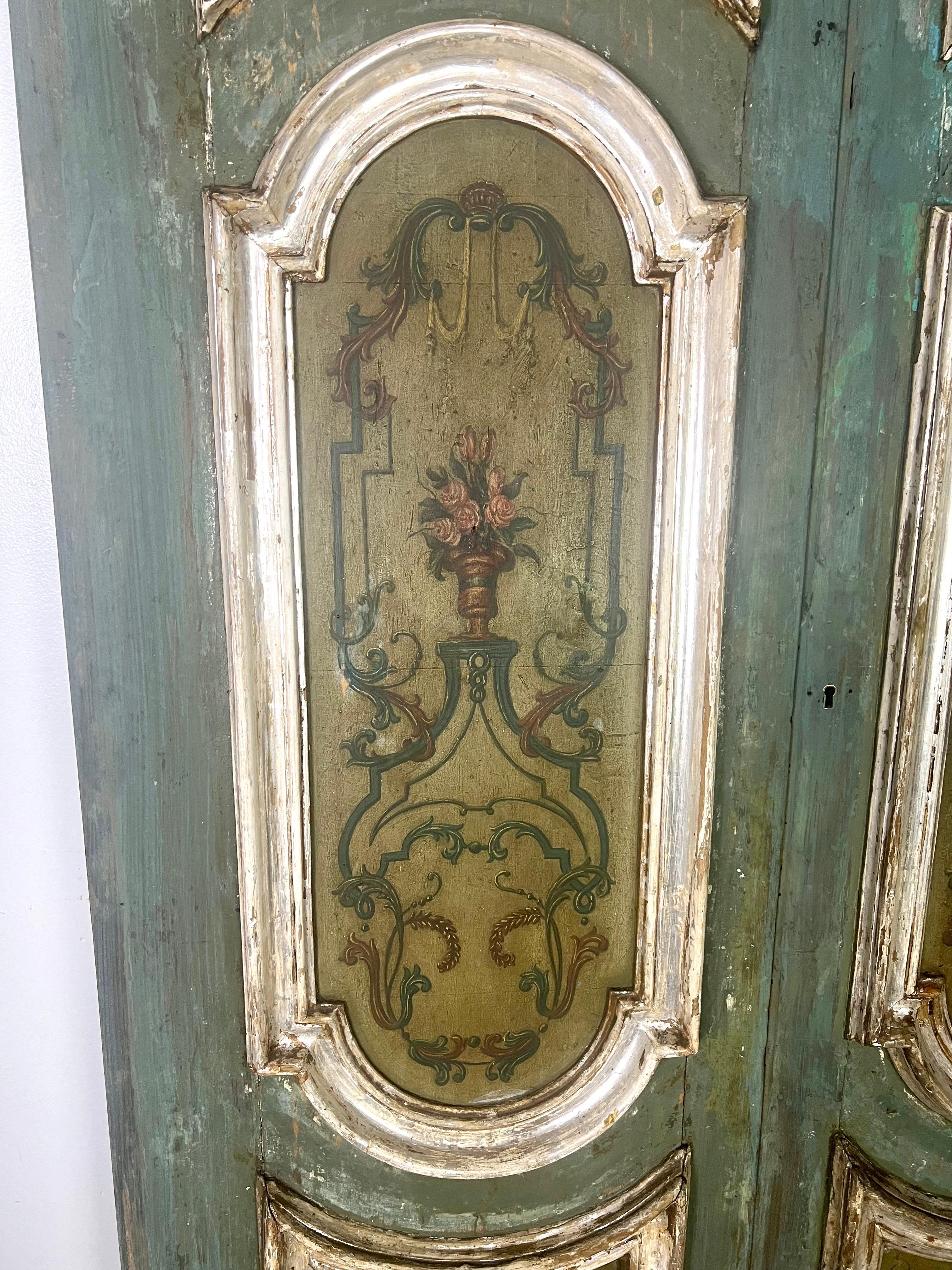 Pair of 19th Century Italian painted & silvered doors featuring a beautiful distressed turquoise finish with golden brown painted panels.  Each panel is ornately painted with floral motifs and framed in elegant silver gilt detailing.  They exhibit a