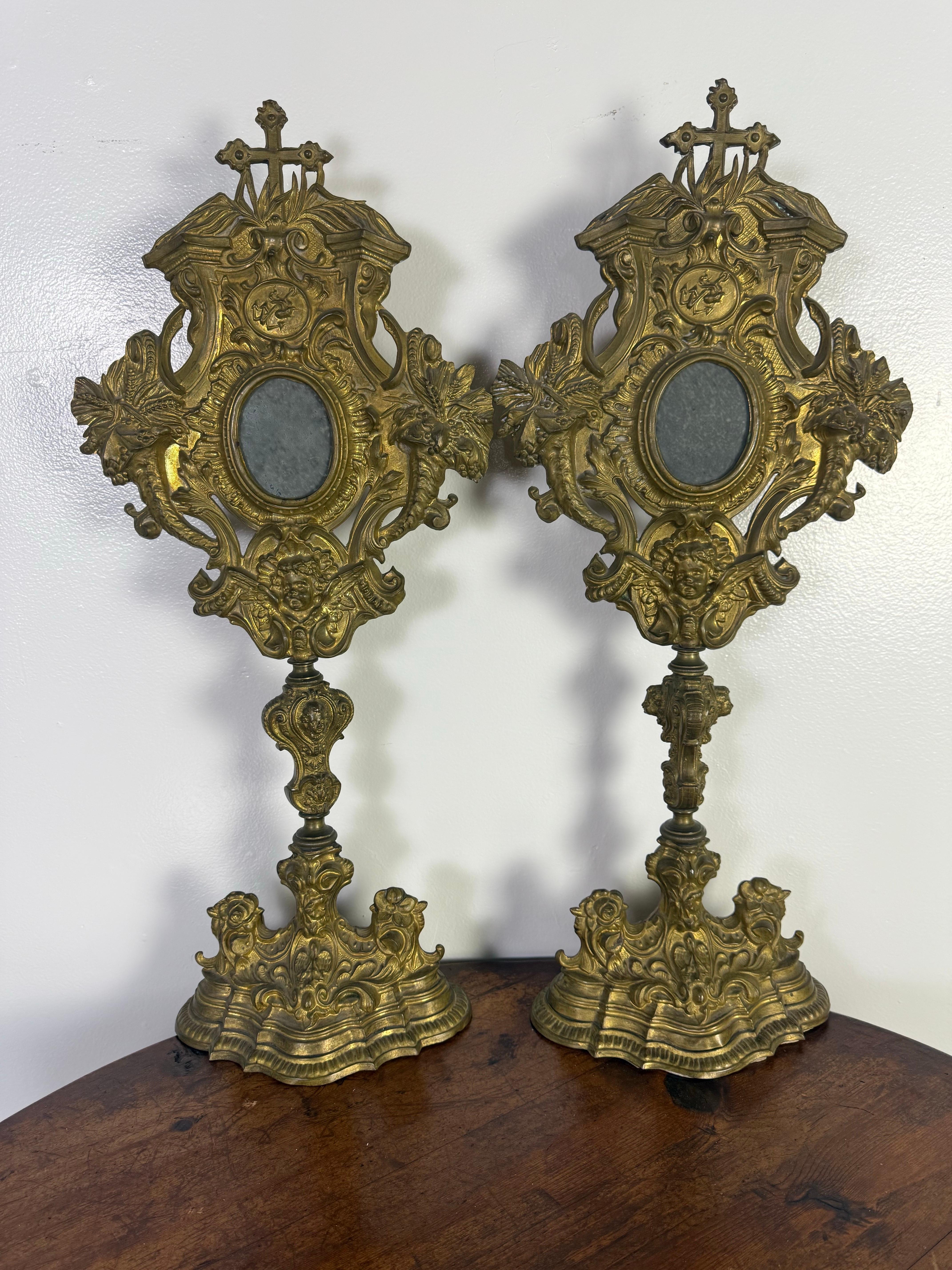 19th century pair of ornate gilded relicquaries made of brass with a gilt finish.  
The feature highly decorative Baroque or Rococo-style detailing, including intricate scrollwork, floral motifs, and cherub faces at the base.  Each piece has an oval