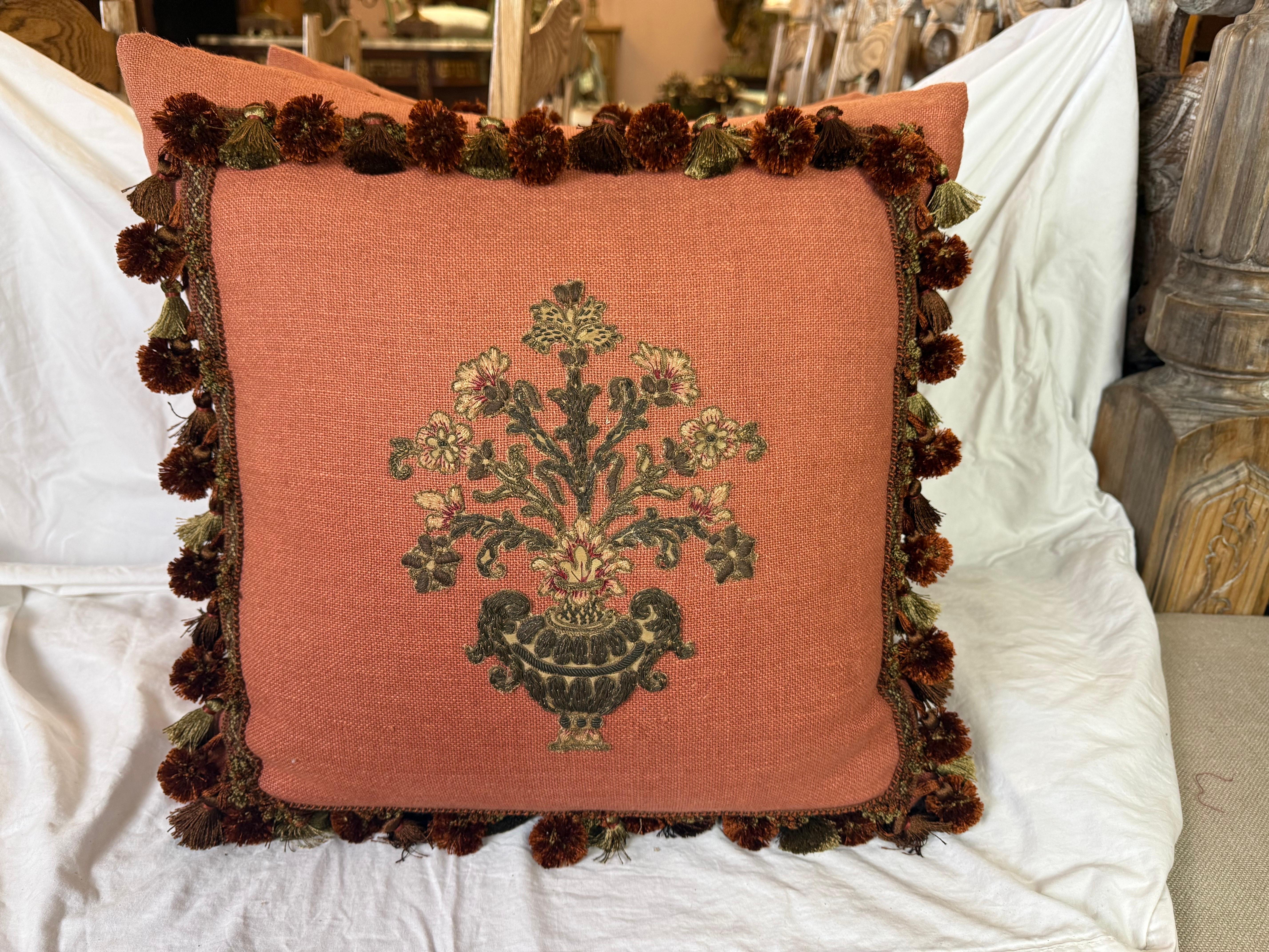 Questi squisiti cuscini sfoggiano un'eleganza senza tempo, con applicazioni ricamate in ciniglia e metallo francese del XIX secolo. Il ricamo è applicato con maestria su un caldo tessuto color terracotta, creando un ricco contrasto che mette in