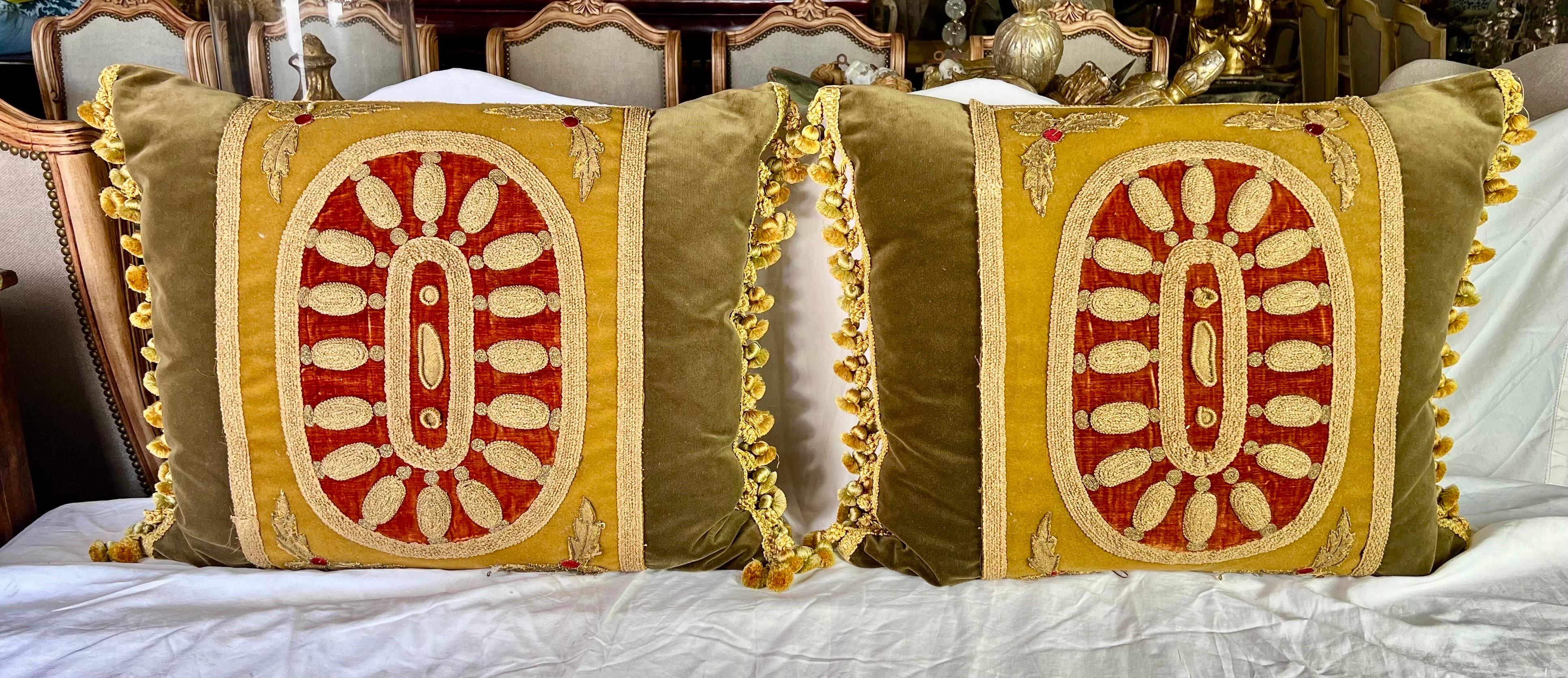 This pair of pillows with 19th-century metallic embroidery on golden velvet, set against a burnt orange background, exude a touch of opulence.  The oval design, green velvet, and multicolored fringe details add to their richness.  Down-filled