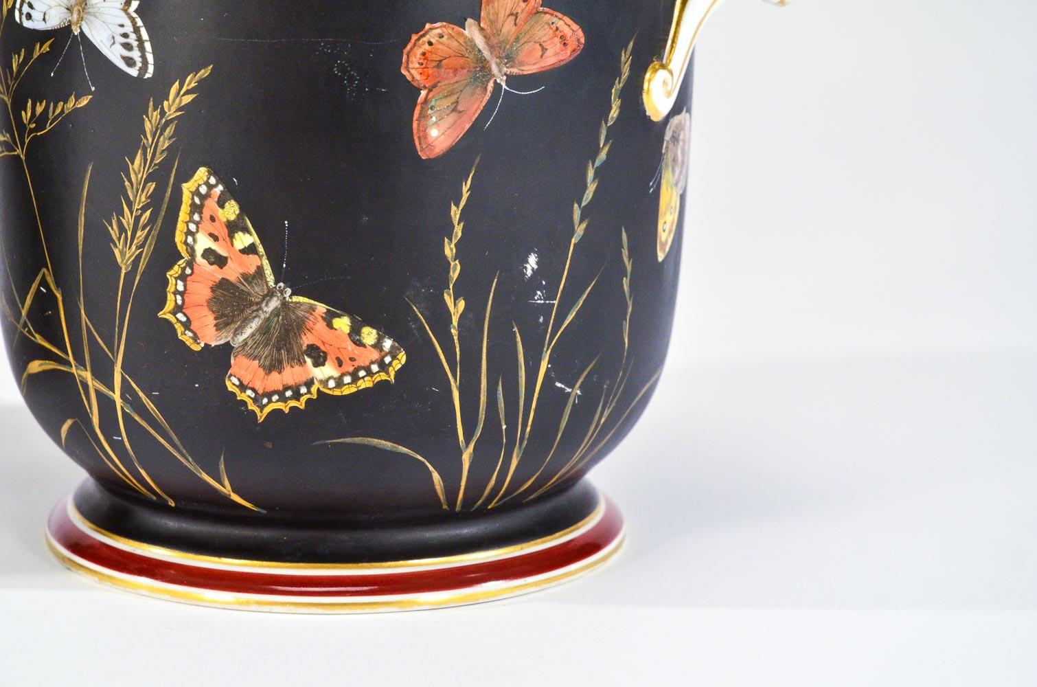 This is an unusually decorated pair of Vieux Paris cachepots in that the body is decorated in a matte black enamel and further embellished with butterflies in flight. The butterflies are interspersed with gold leaves and sheaves of wheat with the
