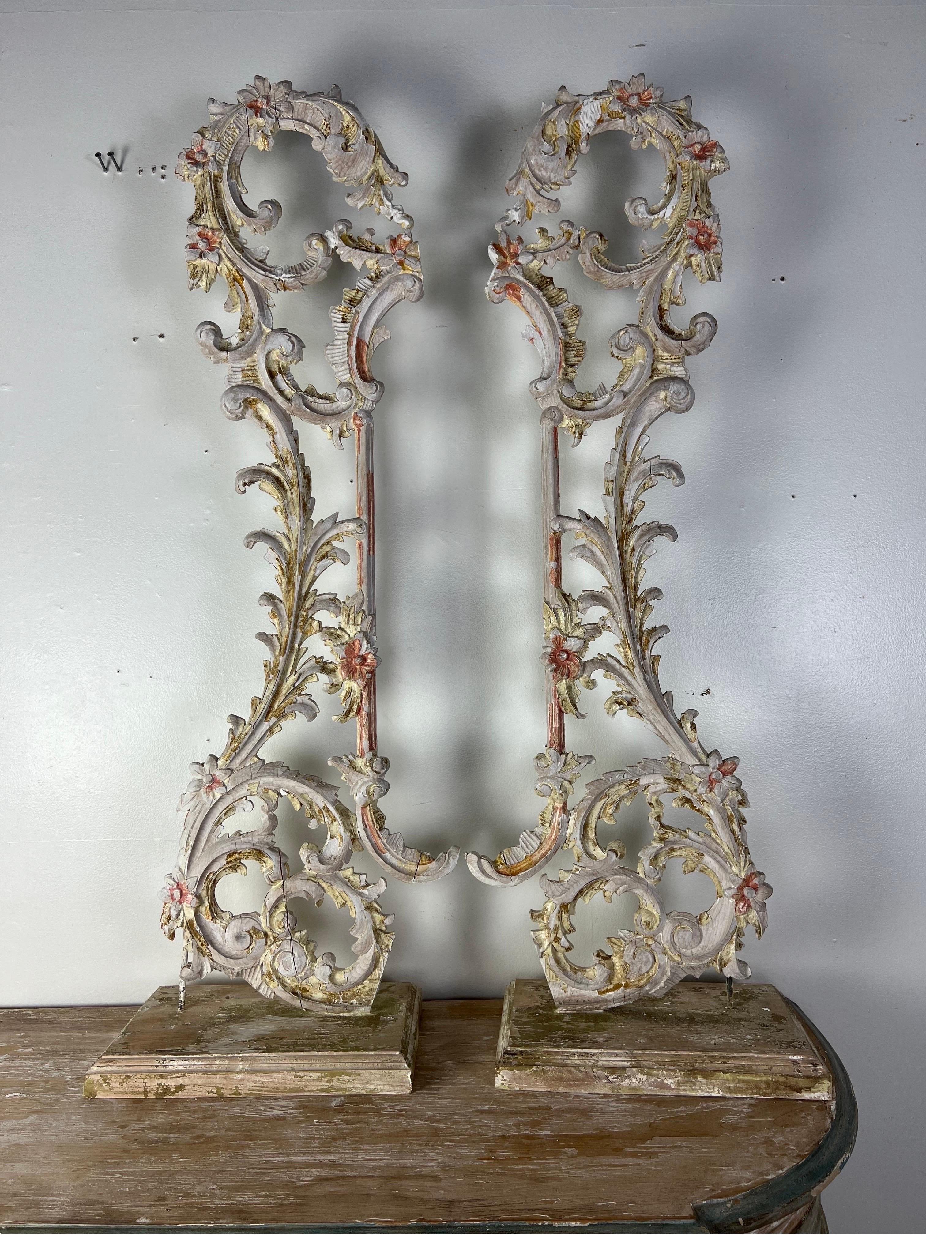 A pair of 19th-century carved Italian architectural elements mounted on wood bases.  The Rococo style carvings showcase intricate detailing, curvilinear forms, and ornate motifs throughout.  These pieces could serve as captivating decorative accents