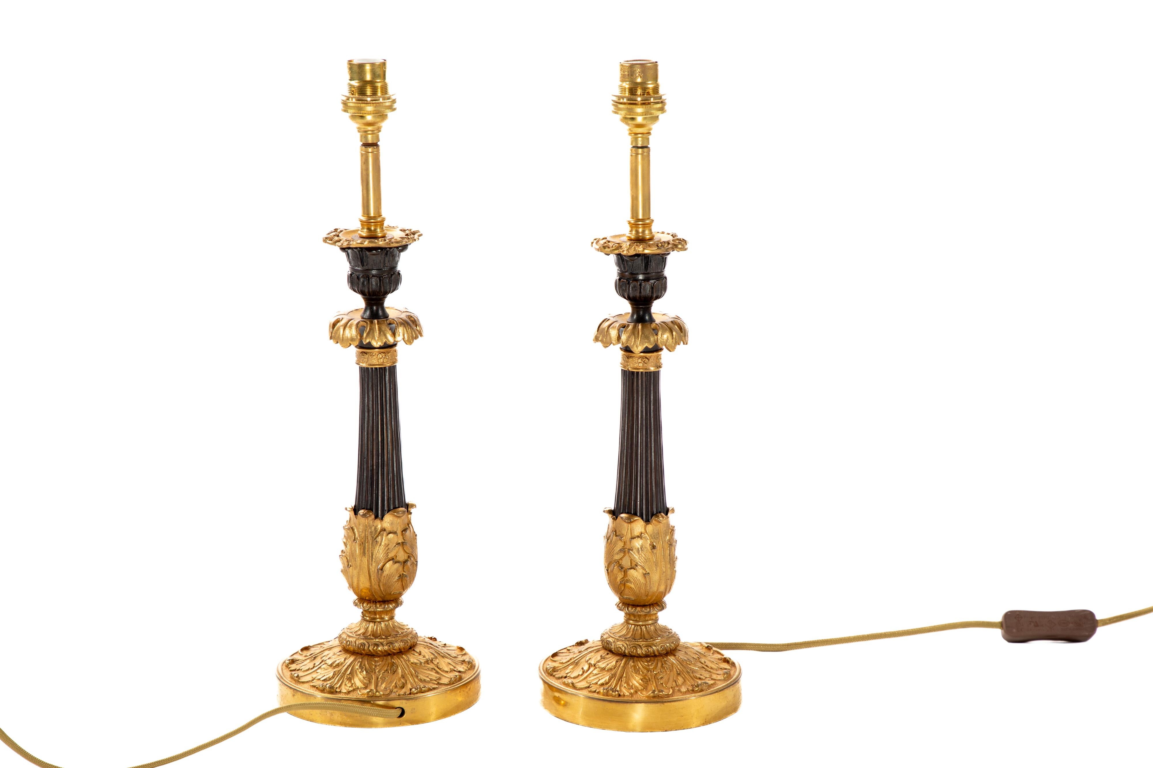 Beautiful pair of 19th century Regency gilt and patinated metal lamps.
Each with an urn candle nozzle and leaf cast pan, on a reeded column with a circular domed foot cast with acanthus.  Converted from candlesticks.  