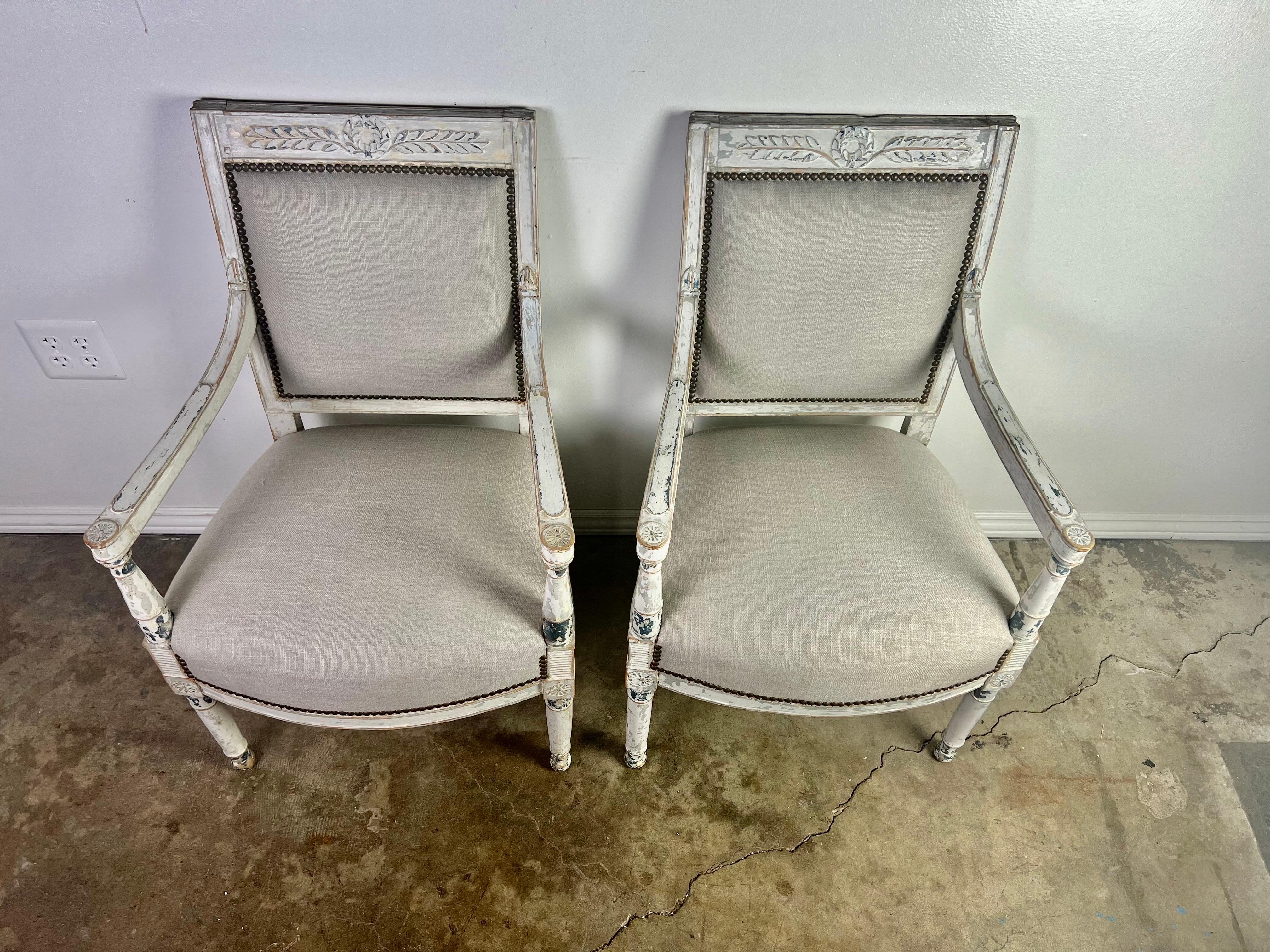 Pair of 19th century Swedish style painted armchairs. The chairs stand on four straight fluted legs. There is a carved laurel leaf design at the top of the chairs. The chairs are newly upholstered in a gray linen with nailhead trim detail. The