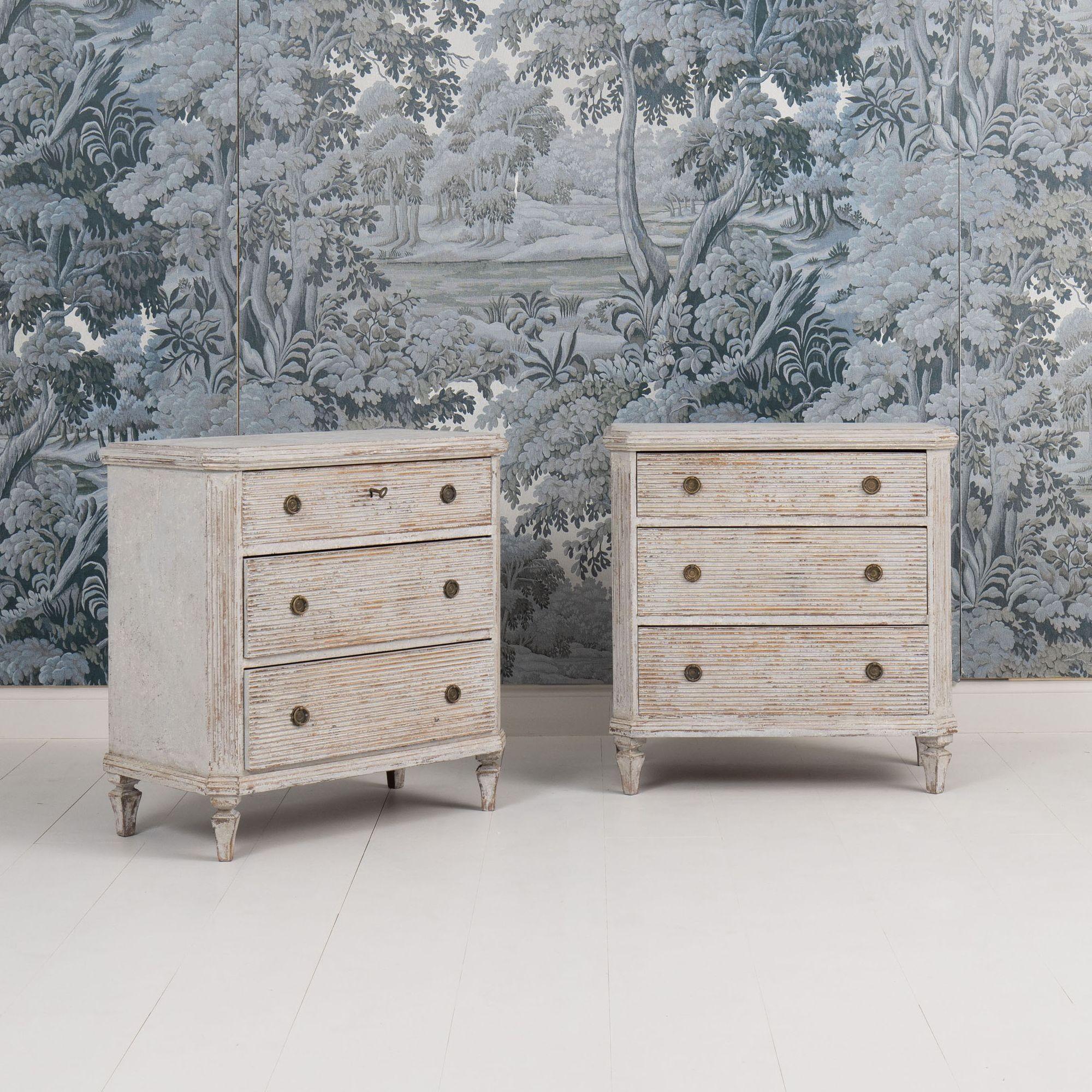 A pair of Swedish Gustavian style commodes in original paint. These chests have beautifully reeded drawer fronts, brass hardware, canted and fluted corner posts, and tapered legs. One key with non-working lock.
