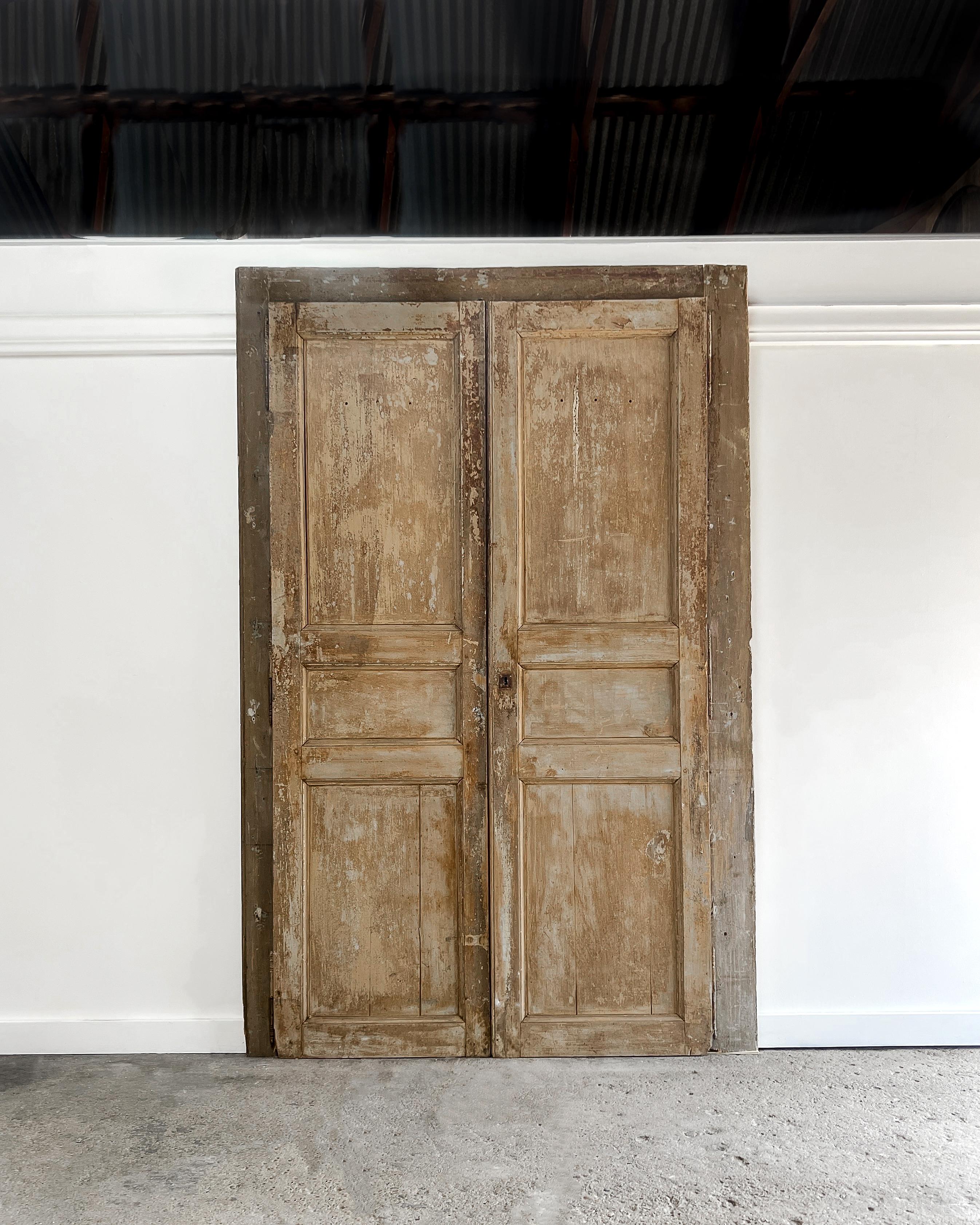 Reclaimed pair of 3-panel configuration French doors with beveled trim detailing. These doors tell a story through layers of earth-tone paint colors, radiating warmth and evoking an irresistible old-world charm. Accompanied by their original